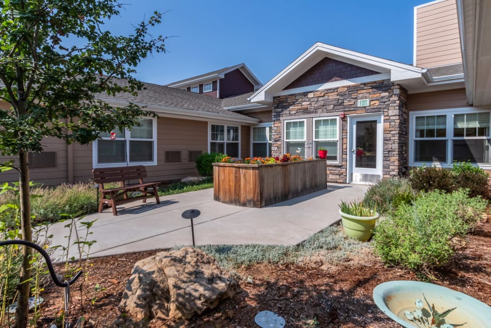 Courtyard of Anthem Memory Care community in Littleton, CO, featuring landscaped gardens, a wooden planter, and a welcoming entrance.