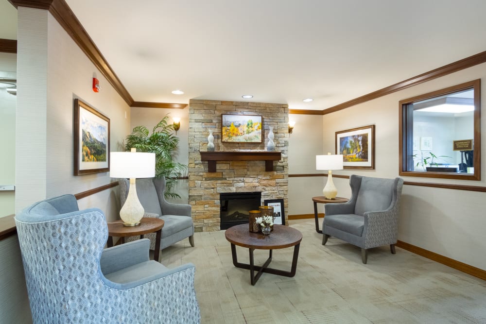 Cozy sitting room in Anthem Memory Care, featuring comfortable armchairs, a stone fireplace, decorative paintings, and a warm atmosphere in Littleton, CO.