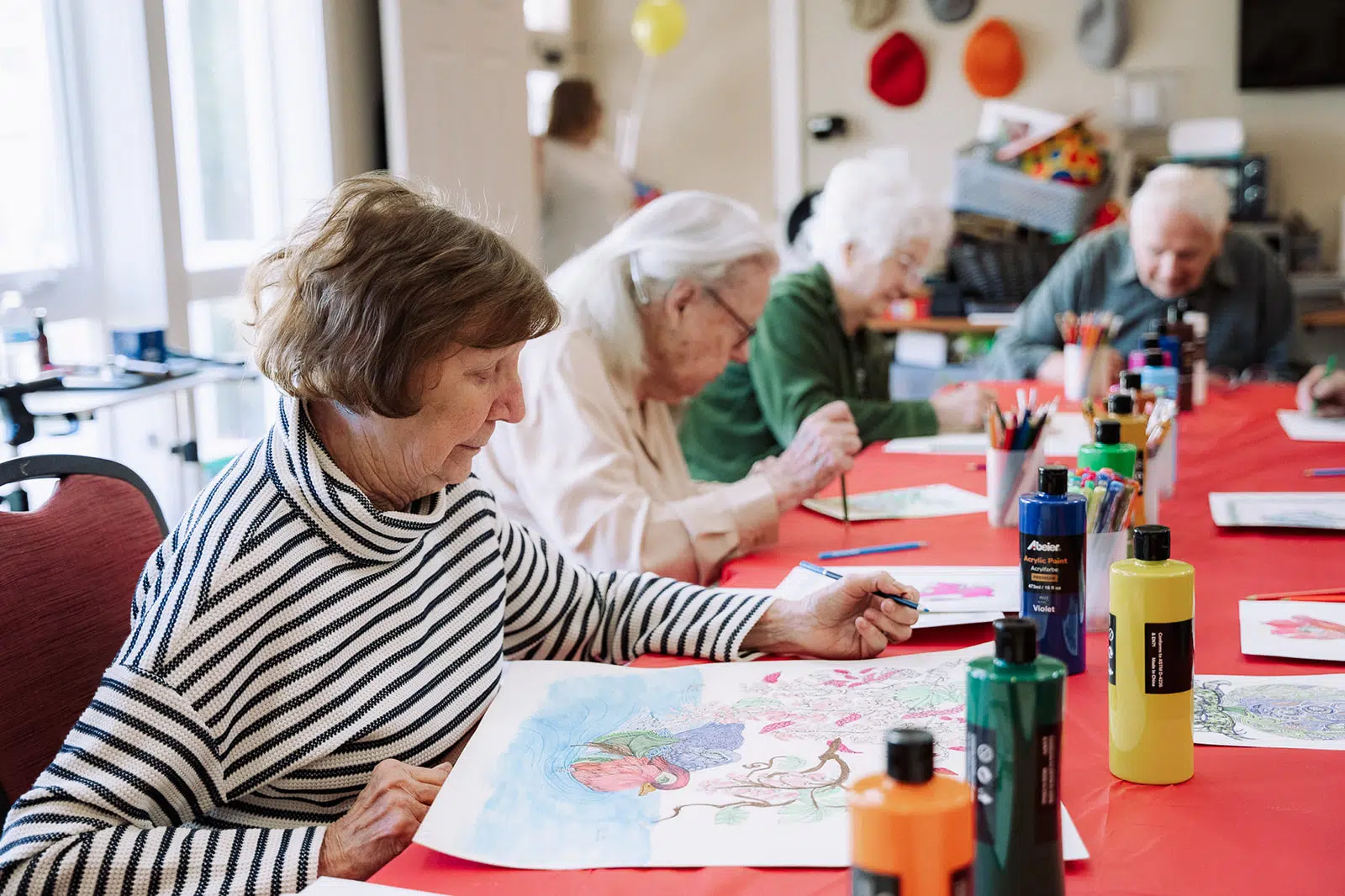 Seniors engaged in an art activity at Concord Place, showcasing creativity with colorful paints and markers on red tablecloth, highlighting memory care and community engagement at Anthem Memory Care.