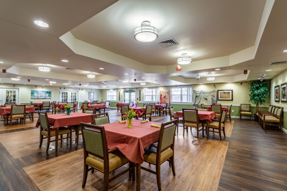 Dining area at Morningside Place Memory Care Community featuring tables with red tablecloths, chairs, and decorative plants, showcasing a welcoming atmosphere for residents.