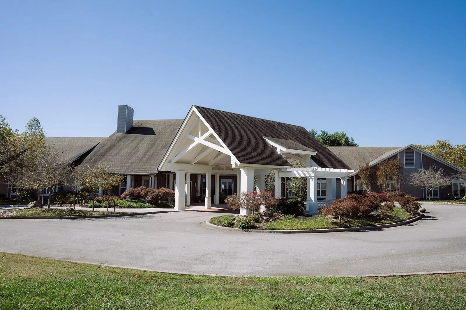 Exterior view of Anthem Memory Care community in Knoxville, TN, featuring a welcoming entrance with a covered porch, landscaped gardens, and a clear blue sky.