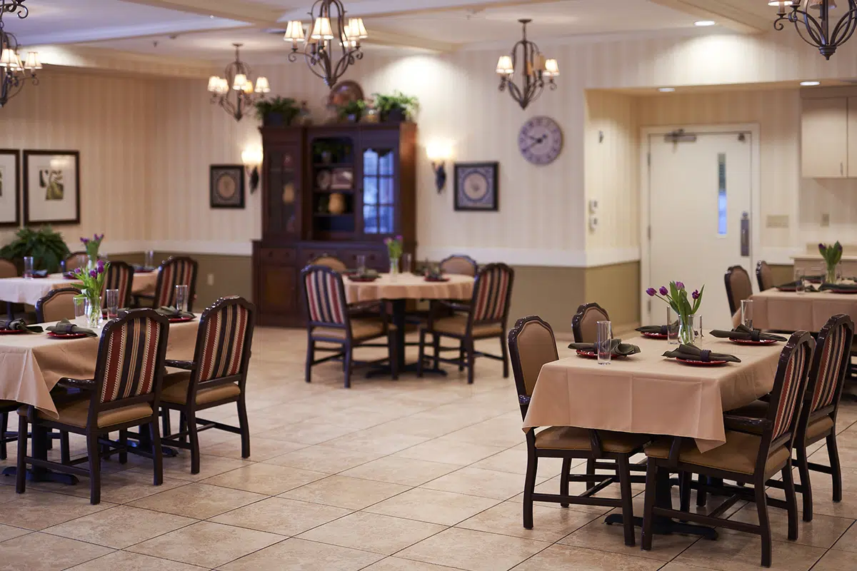 A cozy dining area with several tables set for meals, featuring floral centerpieces and warm lighting.