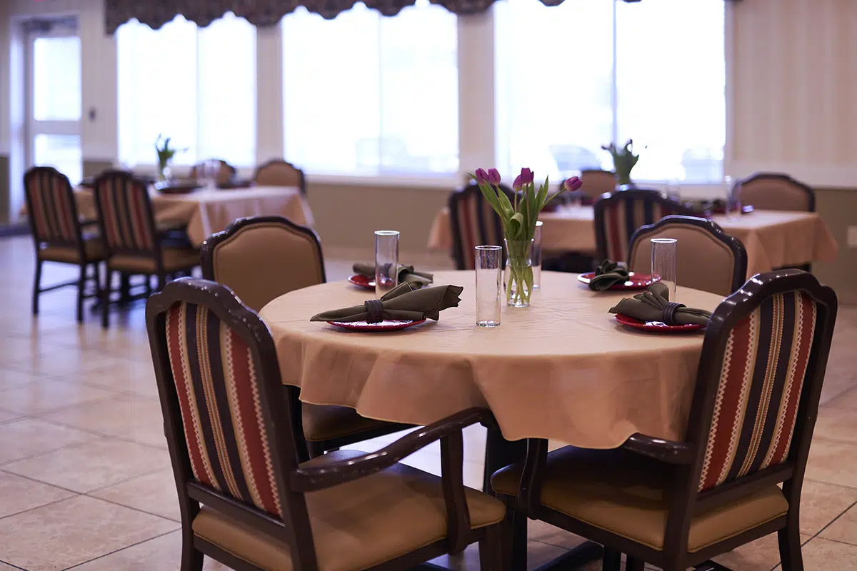 A dining area with round tables set for a meal, featuring beige tablecloths, green napkins, and tulip centerpieces.