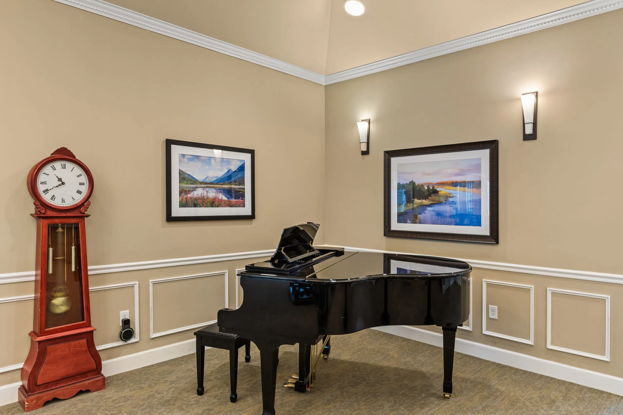A formal music corner with a glossy black grand piano and bench, a large red grandfather clock, and two framed landscape pictures on the beige walls.