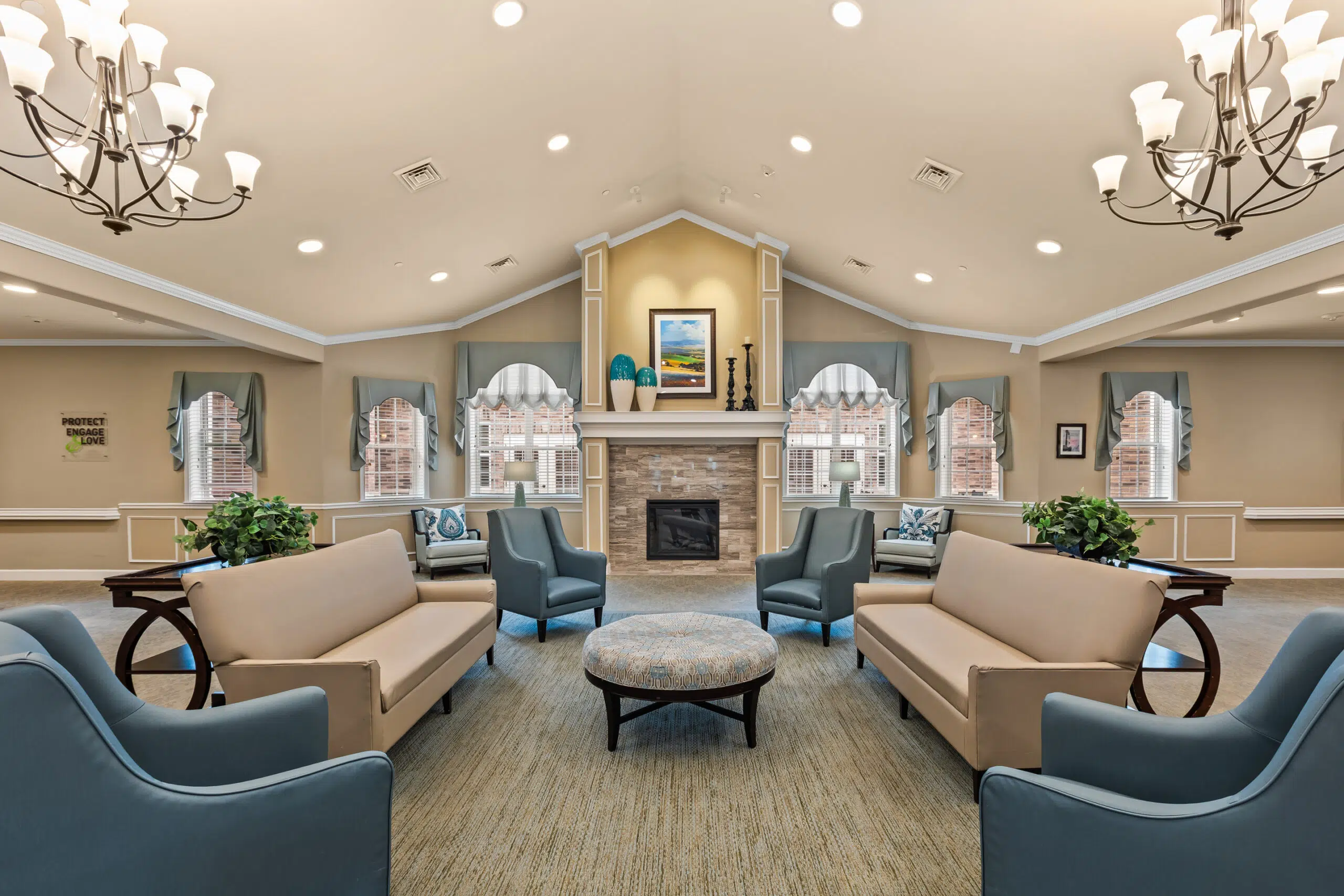 A spacious, symmetrical common lounge area with vaulted ceilings, featuring four distinct seating areas focused around a stone fireplace with a mantle.