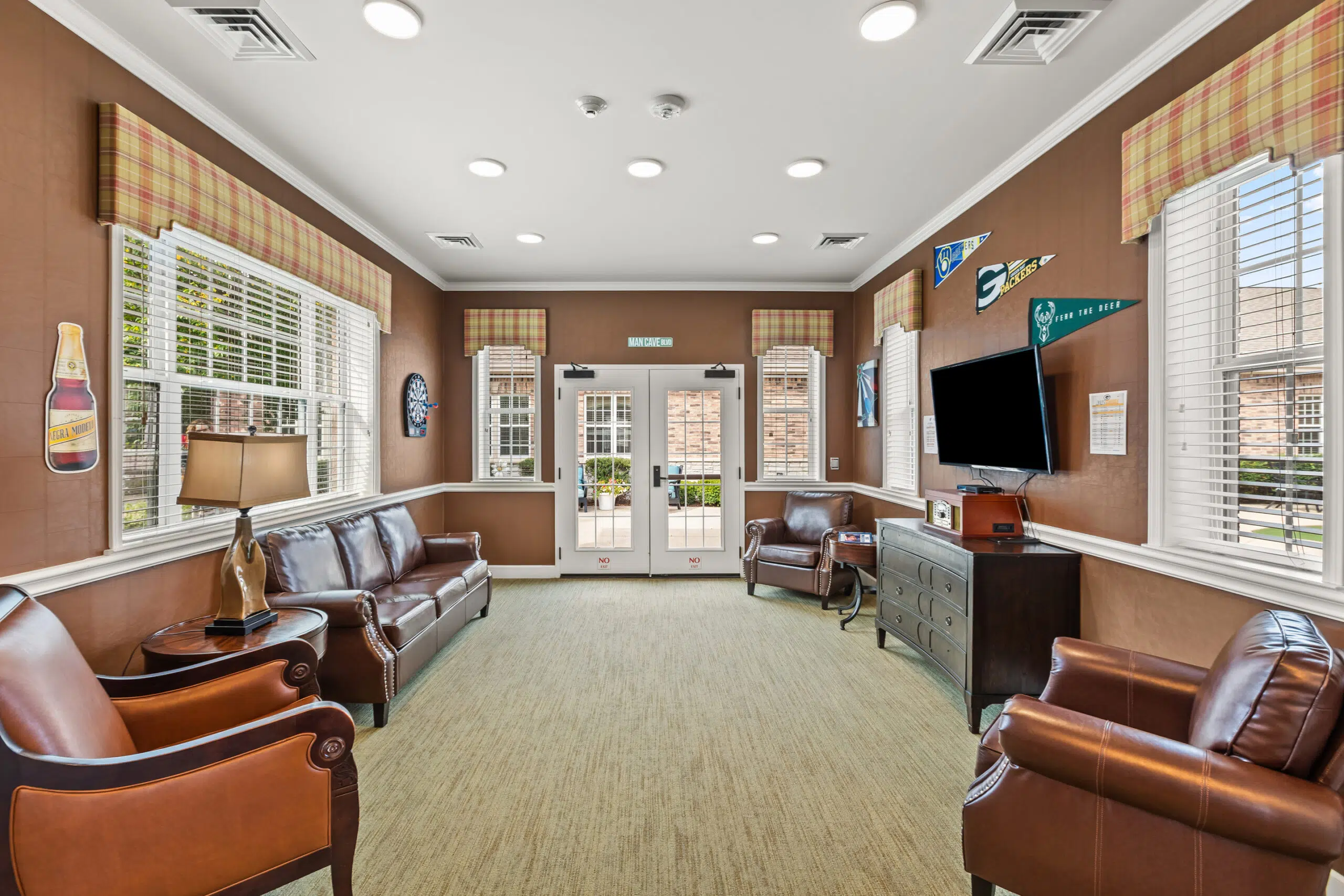 A recreation or lounge room, dubbed a "Man Cave," with brown walls, leather couches and armchairs, a television, and sports pennants and signs on the walls.