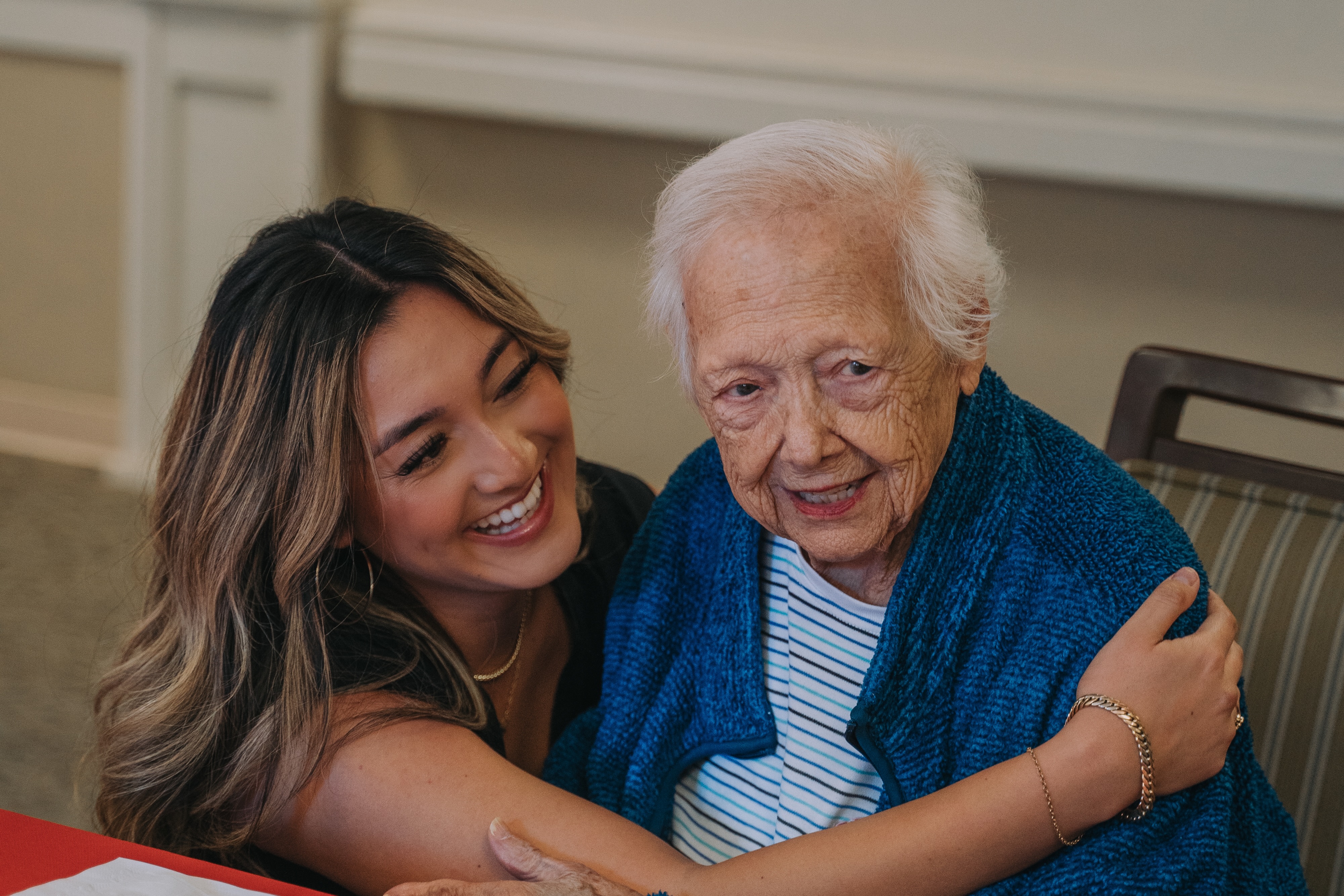 Young woman embracing elderly woman in a cozy setting, reflecting love and connection in a memory care environment.