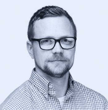 Man with short hair and beard wearing glasses and checkered shirt against a light background.