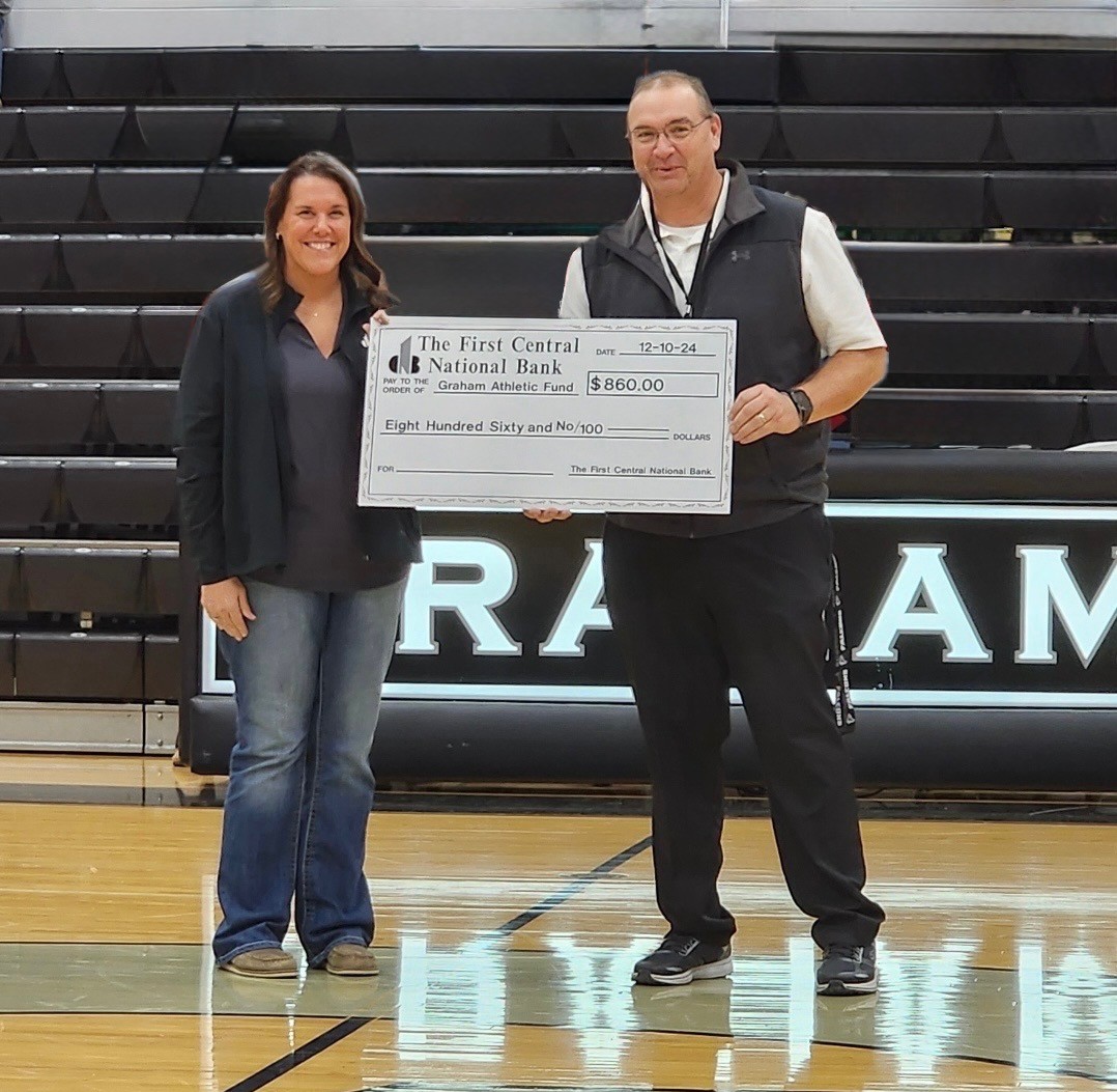 Two people smiling and holding a large check for $860 to Graham Athletic Fund at a gym.