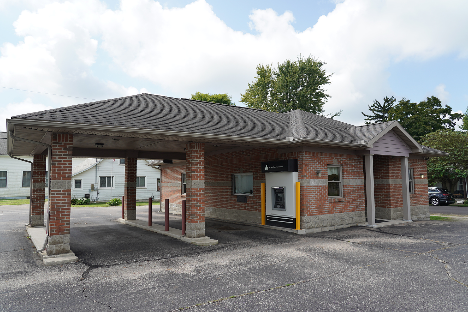Brick building with drive-thru lanes and an ATM machine on a partly cloudy day.