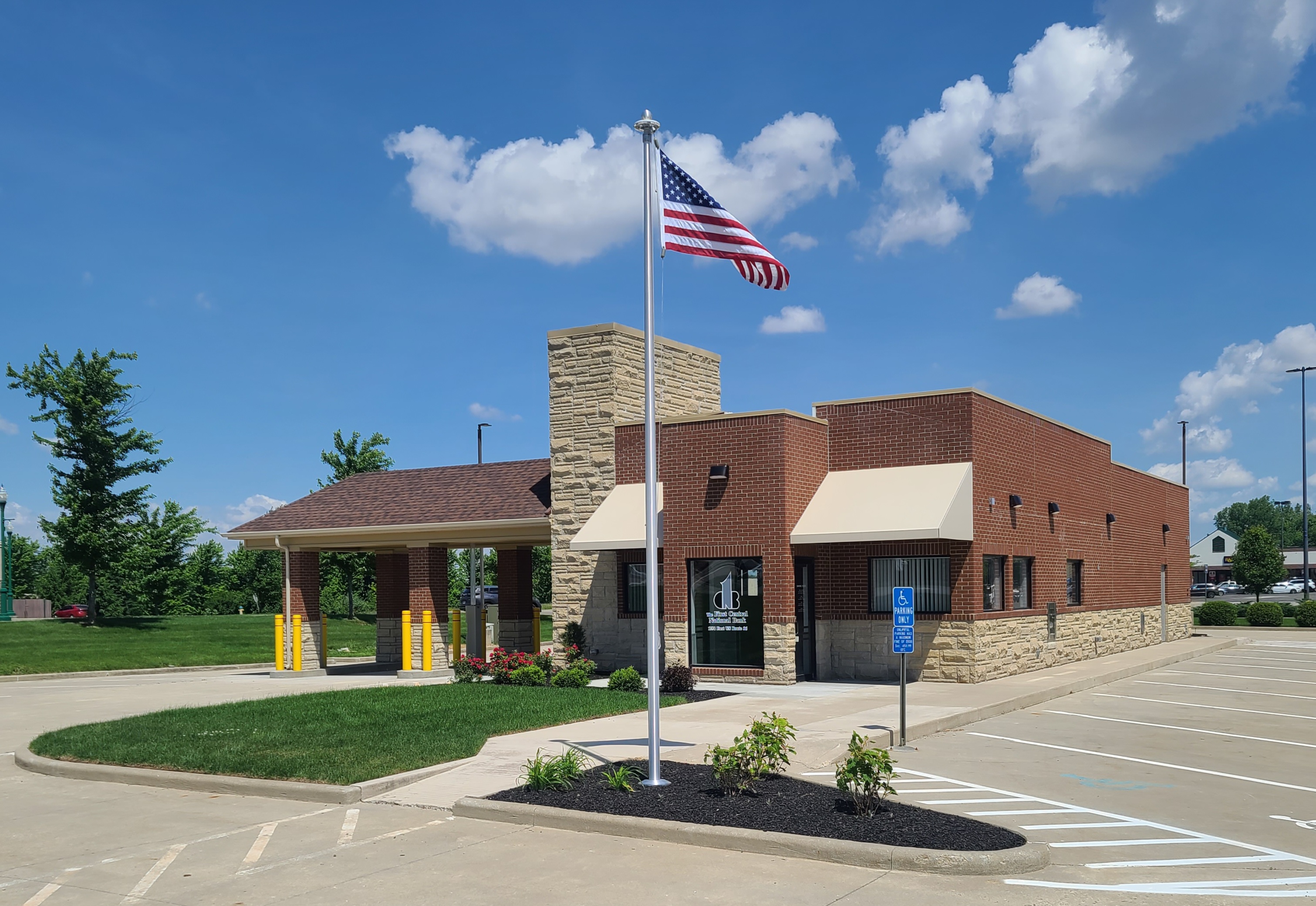Brick and stone community bank building with an American flag on a pole in front and clear blue sky.