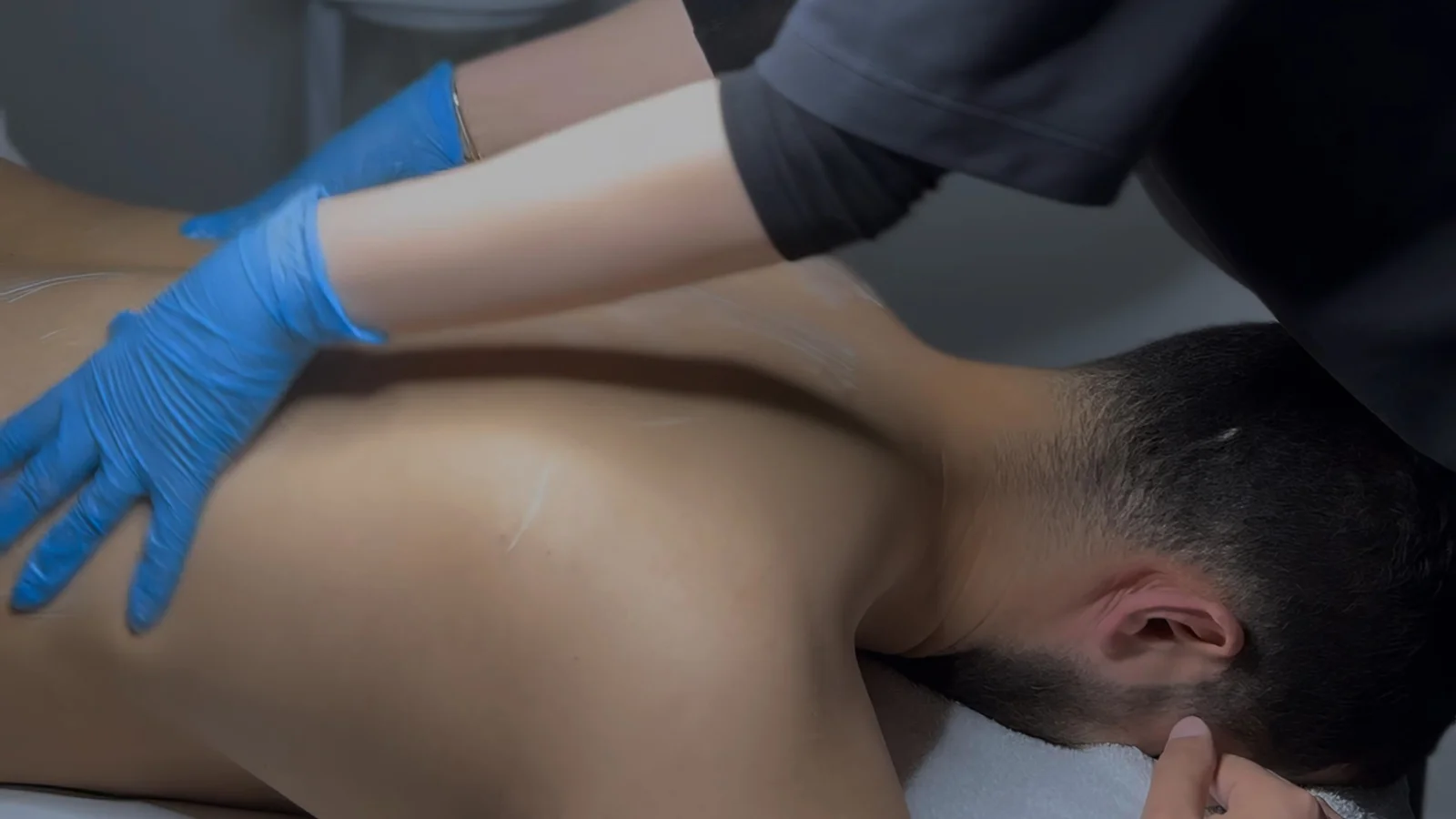 Gloved esthetician cleansing the shoulders and upper back during a back facial treatment