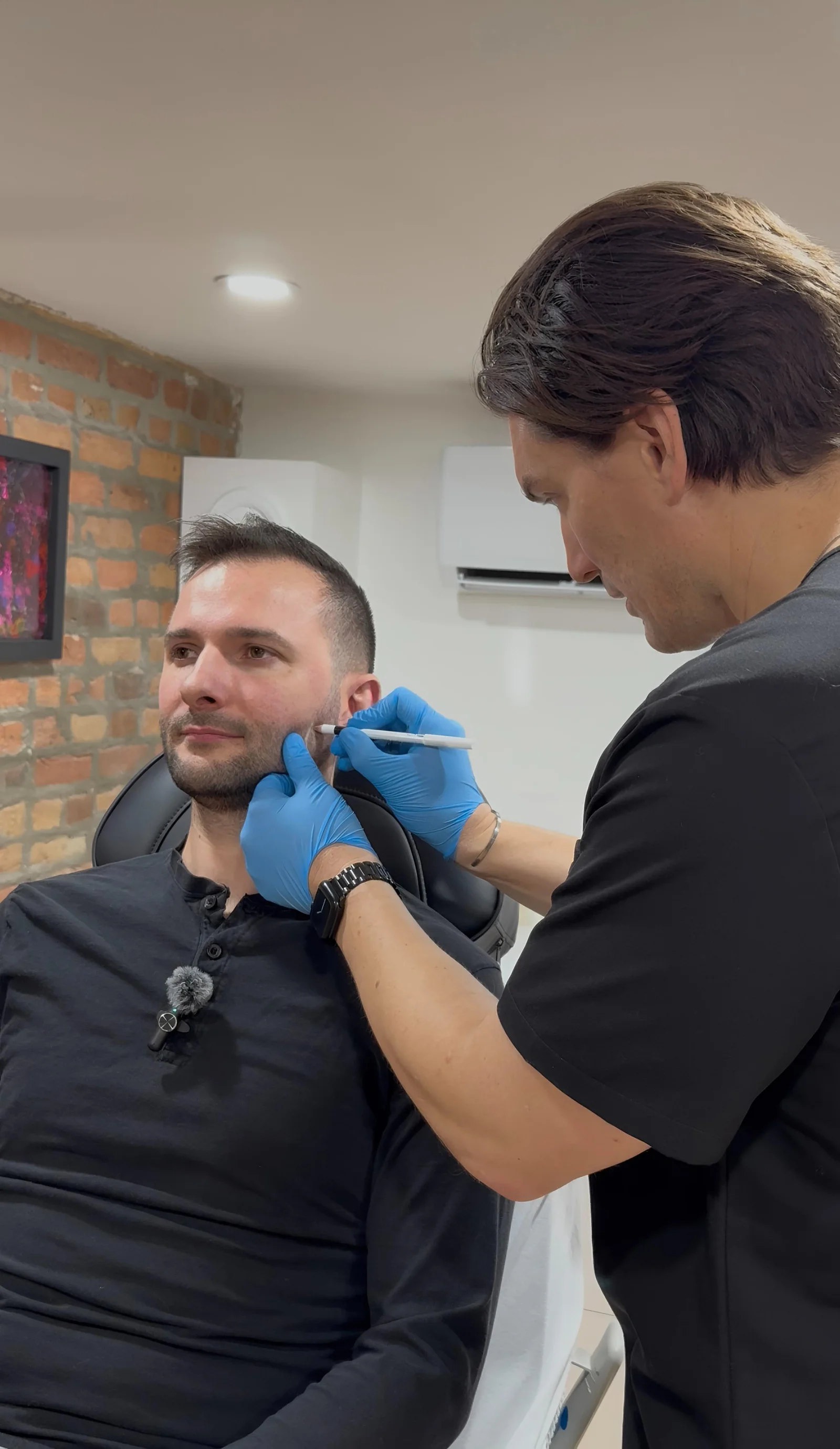 Physician drawing guide marks on a seated male patient's lower face ahead of jawline slimming