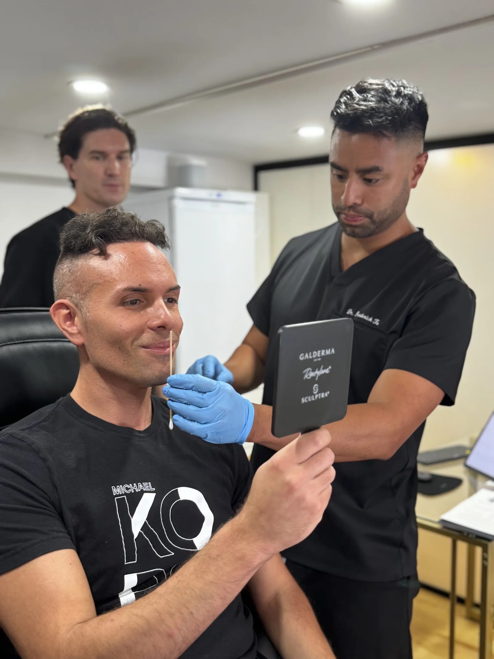 Patient souriant tenant un miroir pendant qu'un médecin marque son visage lors d'une consultation d'affinement de la mâchoire