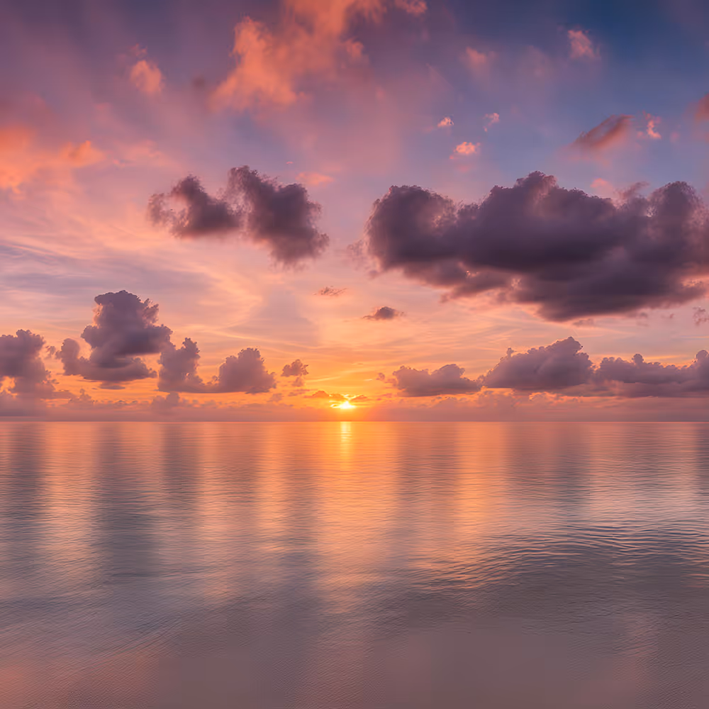 Sunset over calm ocean with dramatic clouds reflecting pink and orange light on water.