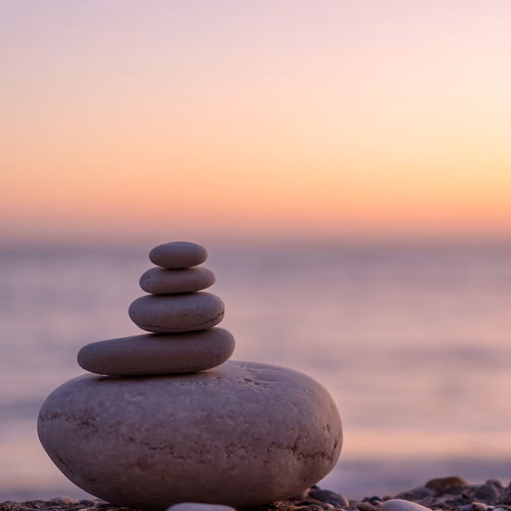 Stack of smooth stones on a beach with a pastel sunset and calm sea in the background.