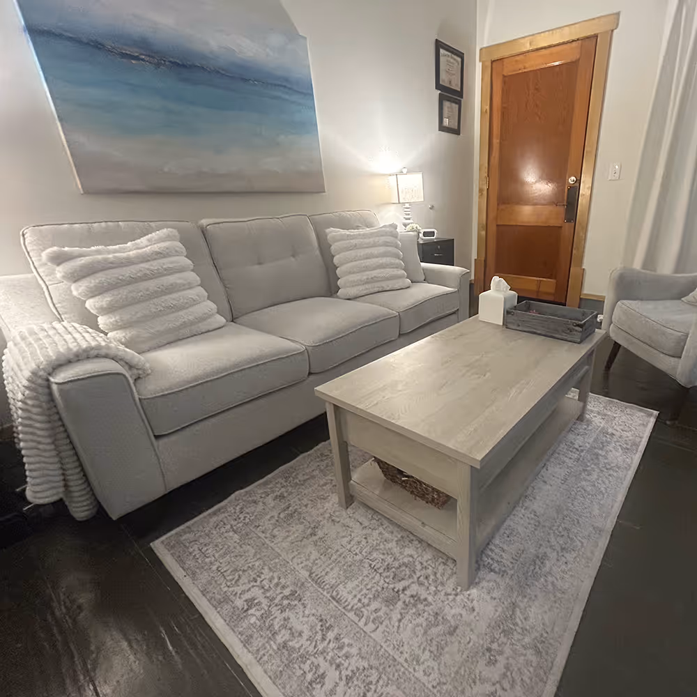 Cozy living room with gray sofa, matching armchair, wooden coffee table, and abstract blue wall art.