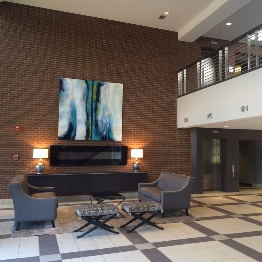 Modern lobby with brick wall, two gray sofas, two patterned stools, and abstract wall art.