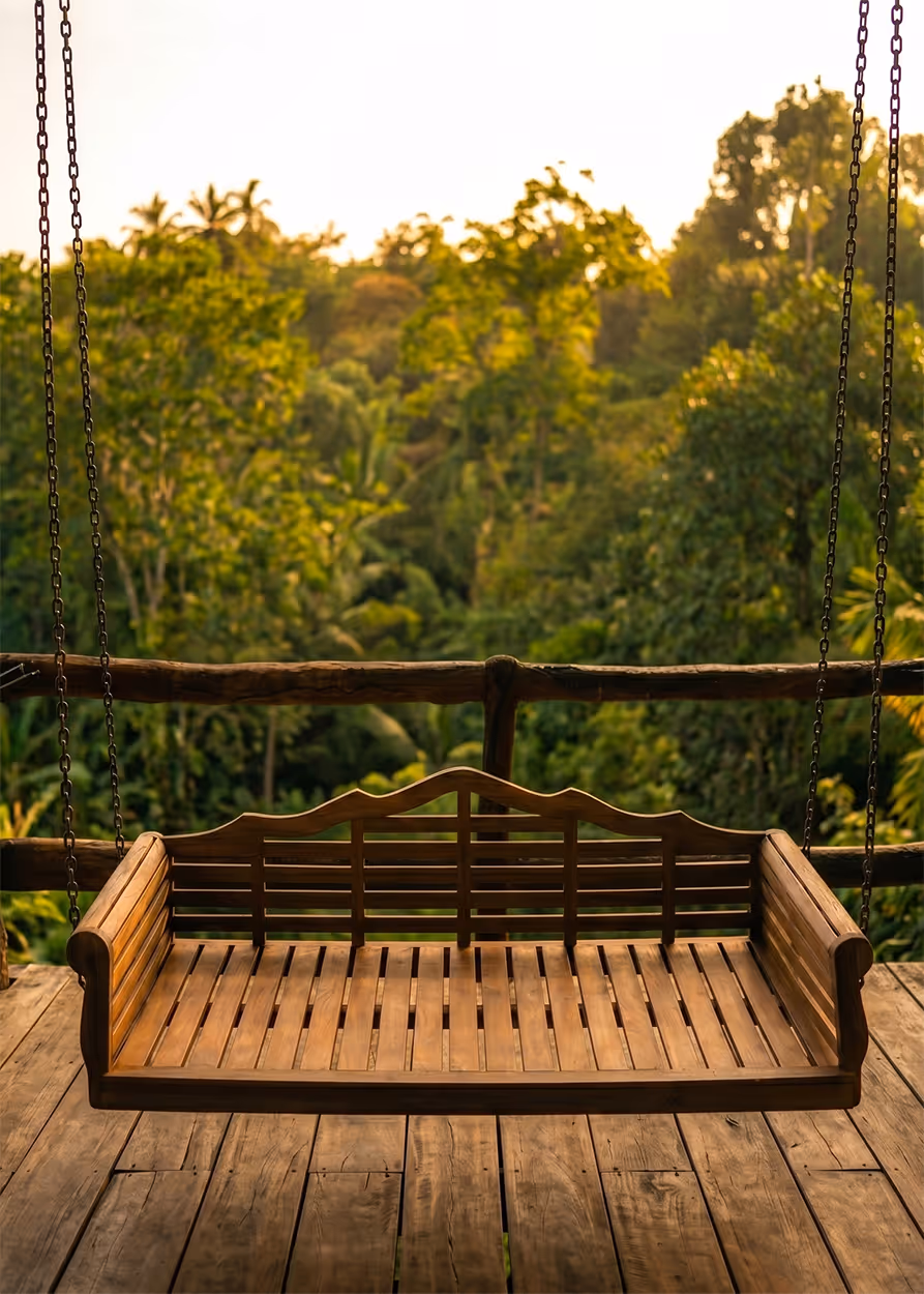 Empty wooden porch swing hanging by chains with green trees background at sunset.