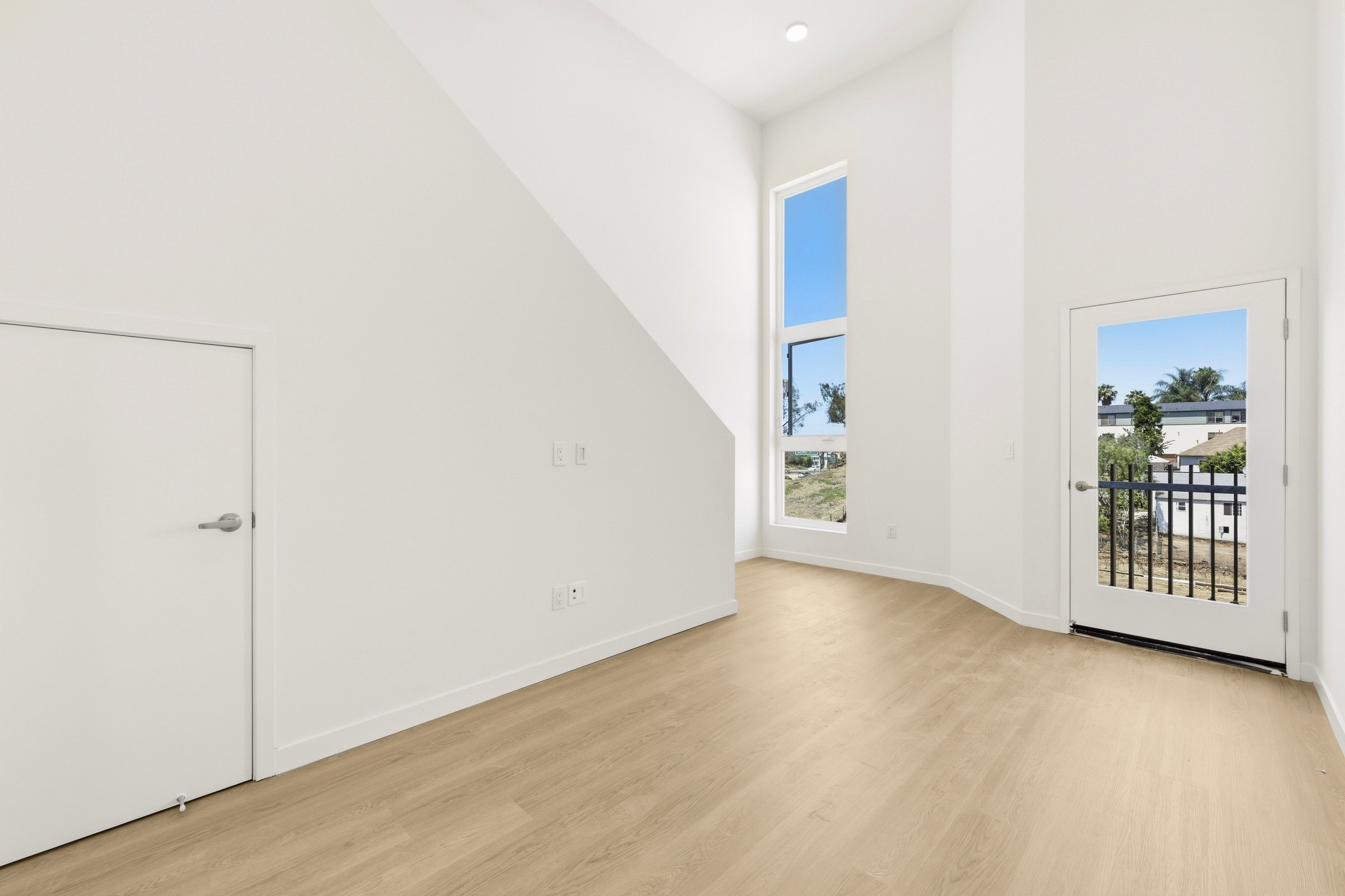 Bright unfurnished Goldilocks apartment living area with wood-style flooring, high ceilings, and a private balcony.