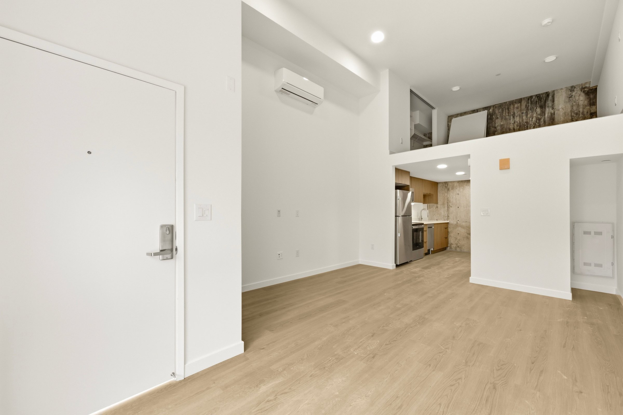 Open Goldilocks apartment interior with a modern kitchen, light wood flooring, and an entry area.
