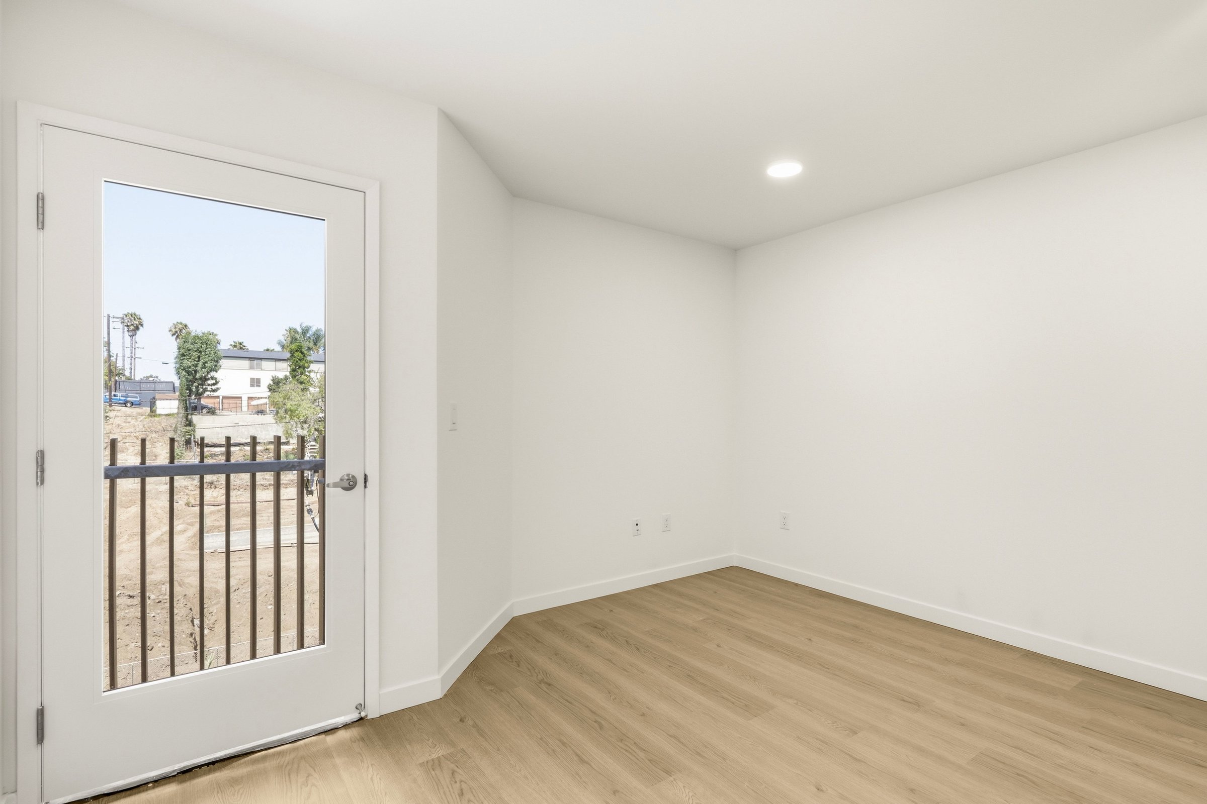Bright Goldilocks apartment bedroom with light wood flooring and direct access to a private balcony.