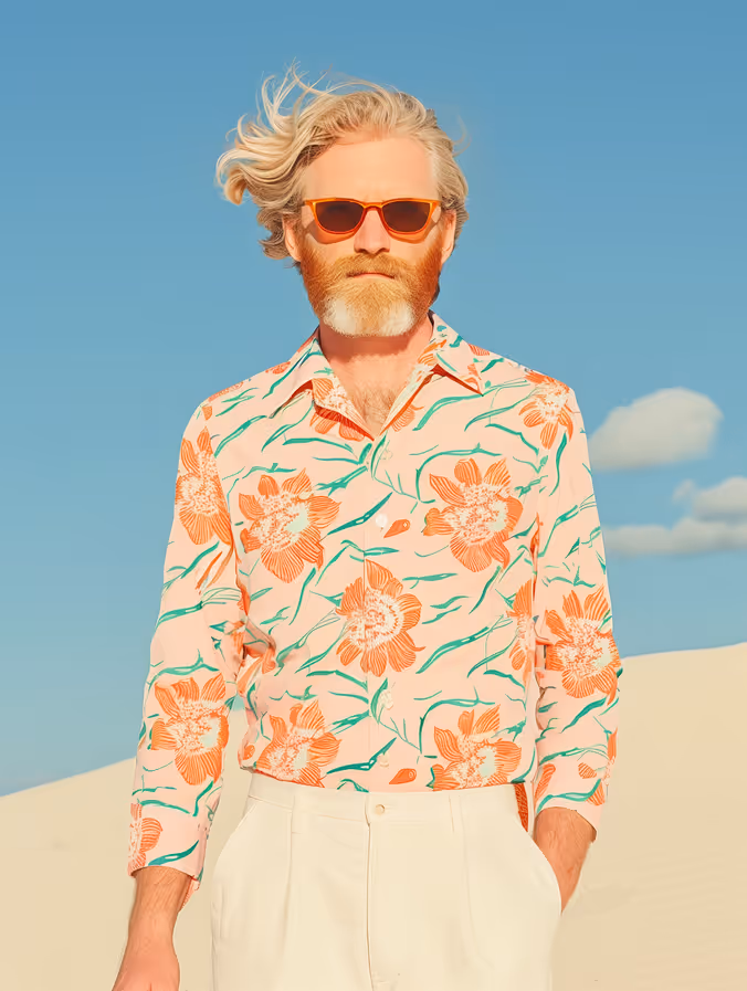 Man with orange beard and sunglasses wearing a floral shirt and white pants under a clear blue sky.