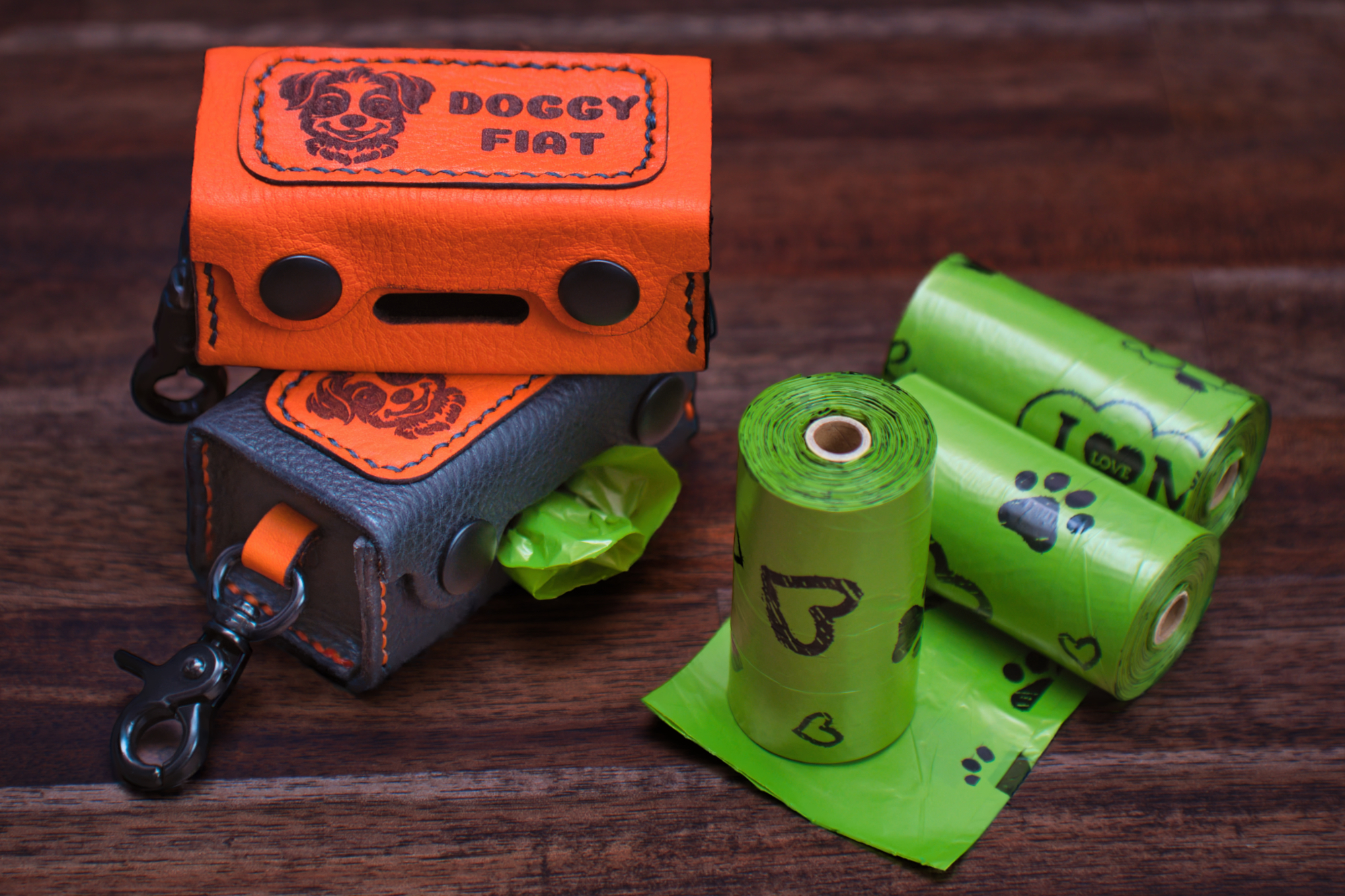 Two Doggy Fiat leather holders with clips and three rolls of green dog waste bags with paw prints and hearts.