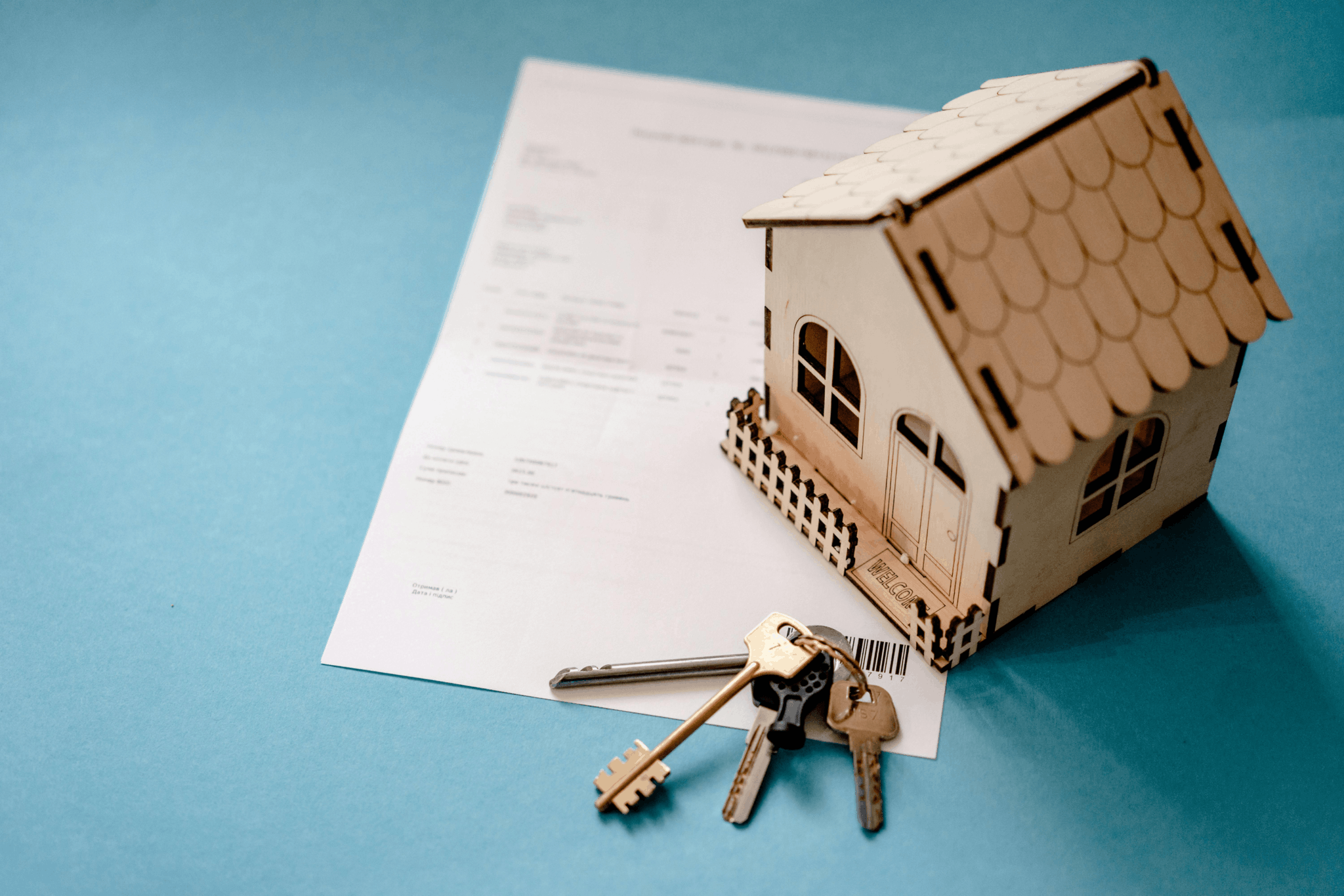 House keys on a mortgage document beside a small wooden house