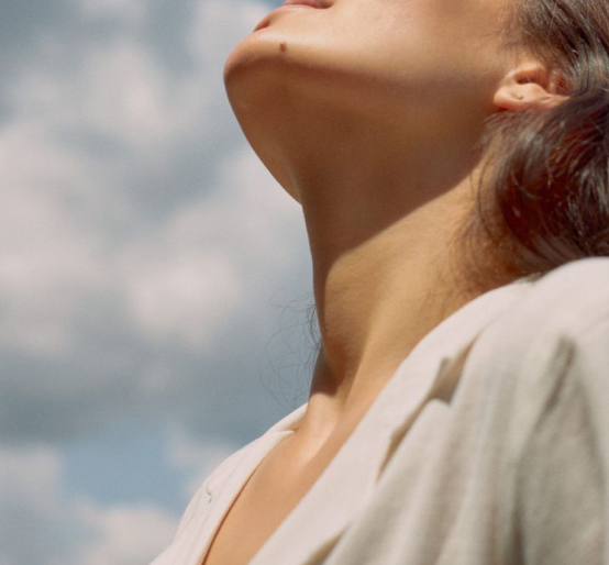 Person standing outdoors with eyes closed, taking a deep breath in a peaceful setting