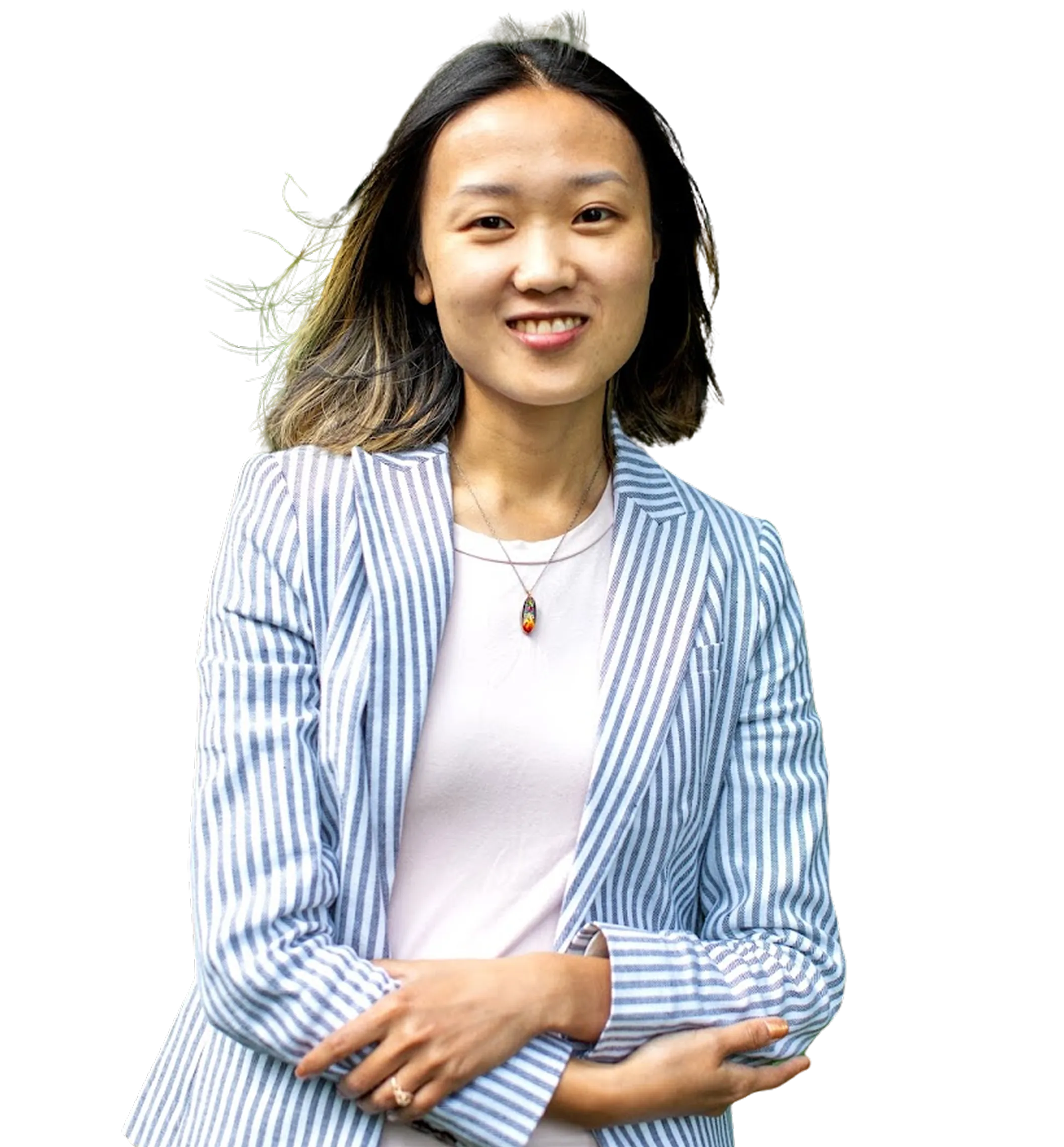 Young woman with straight hair wearing striped blazer and white shirt, smiling with arms crossed.