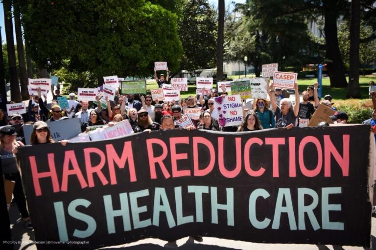 Advocates march with a banner reading Harm Reduction Is Health Care
