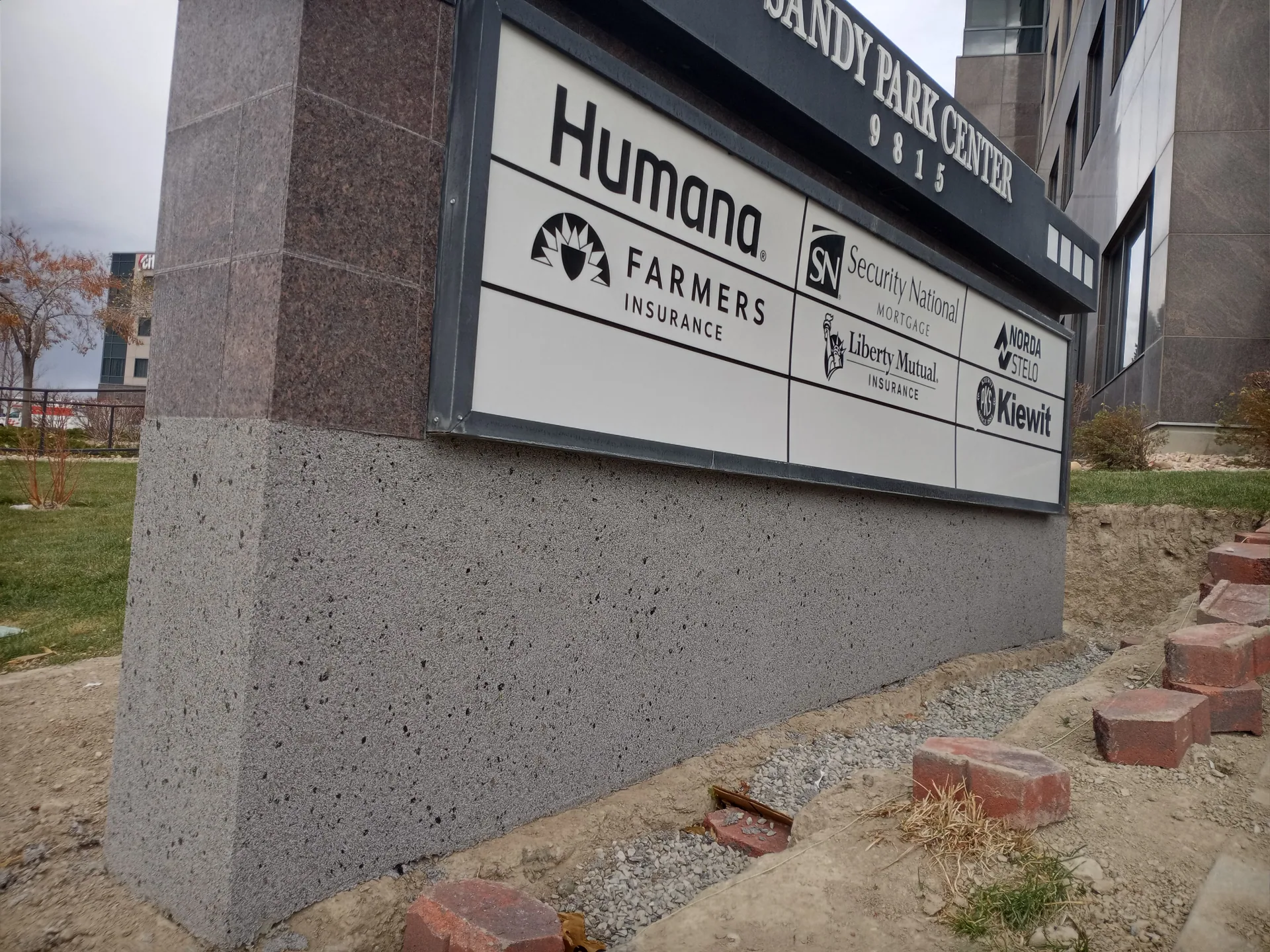 Outdoor sign base for Sandy Park Center listing companies like Humana, Farmers Insurance, Liberty Mutual, and Kiewit.