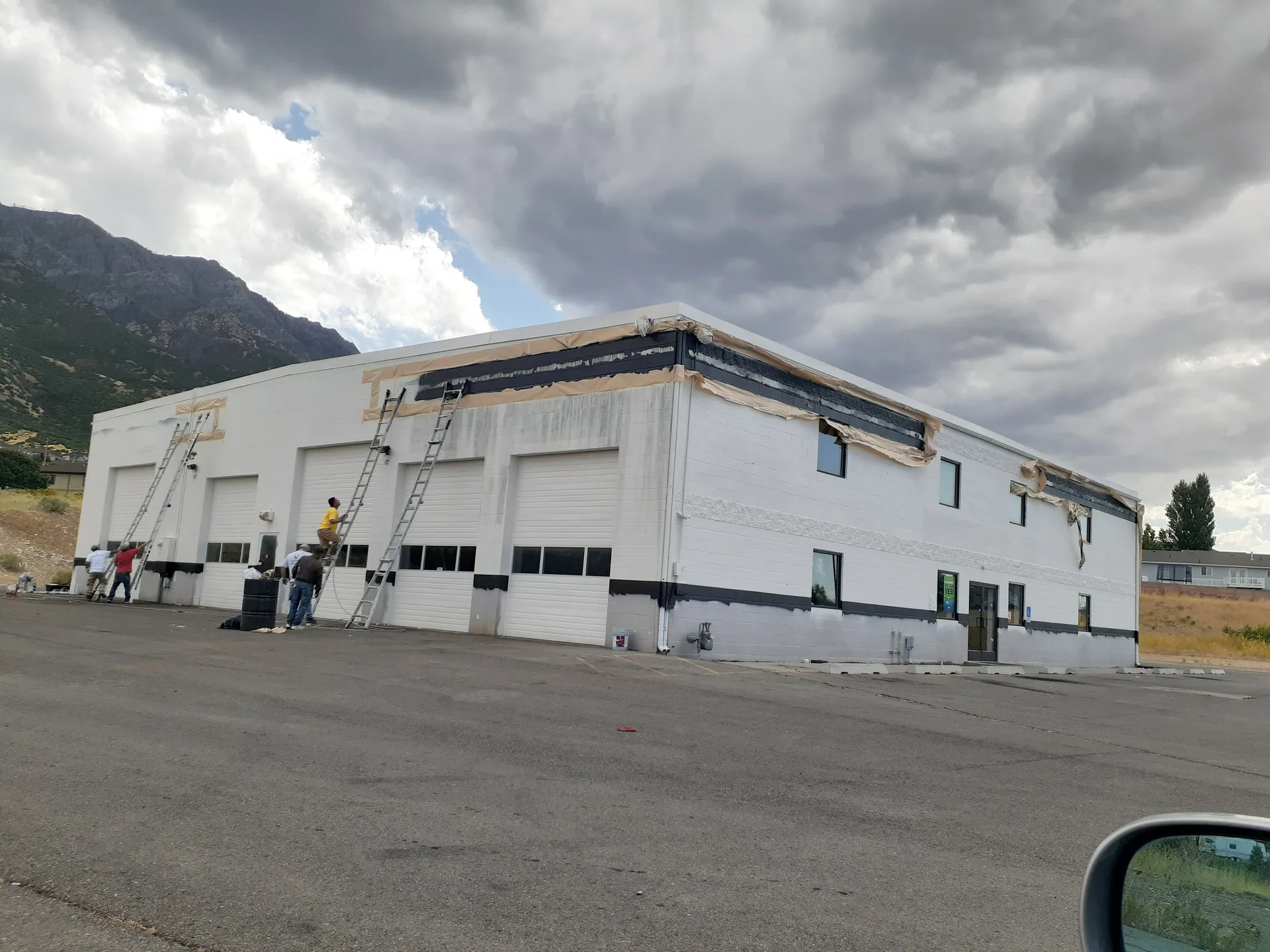 Several workers on ladders painting black stripes on a white industrial building.