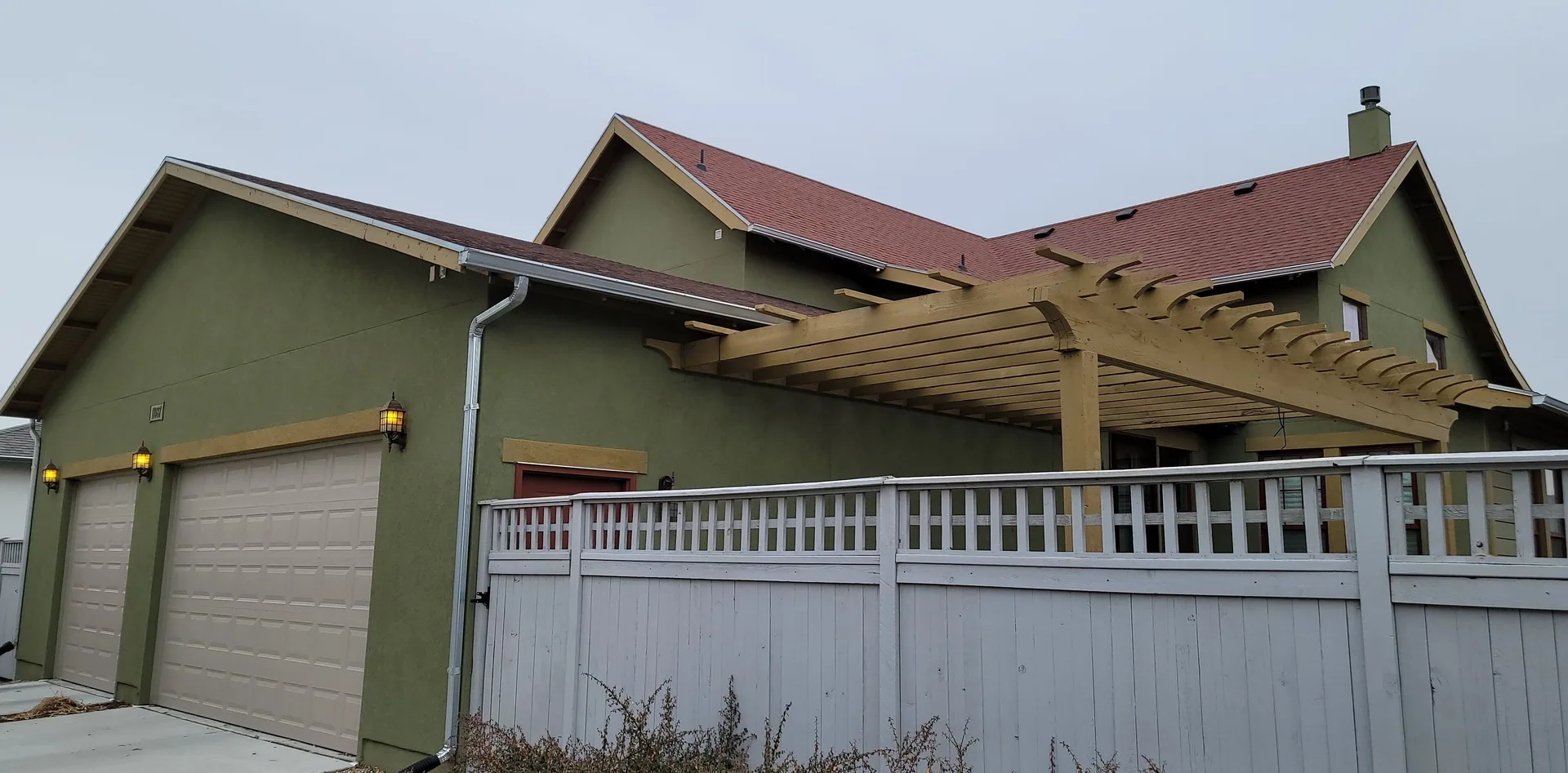 Green two-story house with a red roof and wooden pergola.