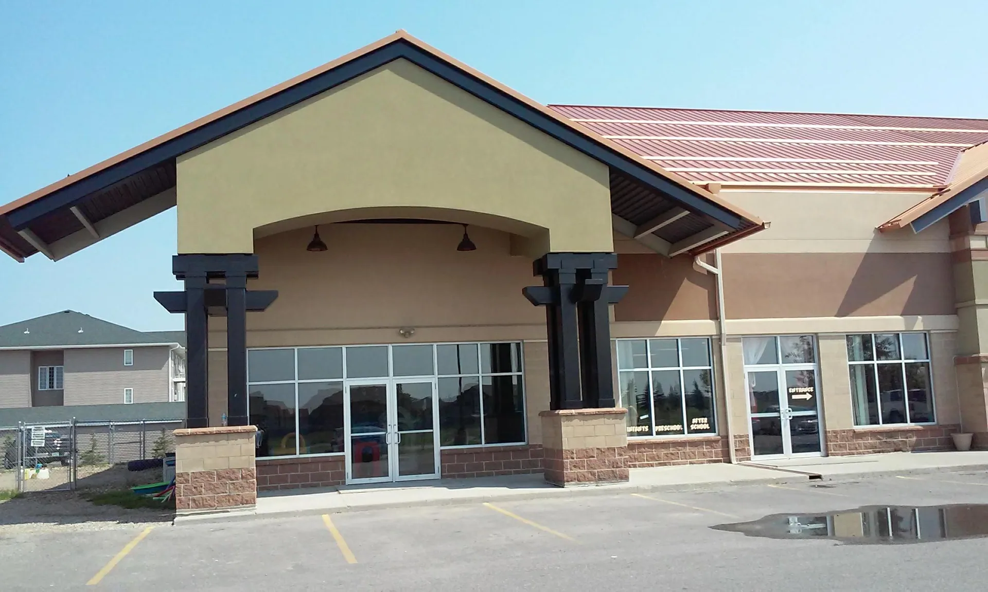 Modern building entrance with large windows, double glass doors, and a covered portico supported by dark columns.