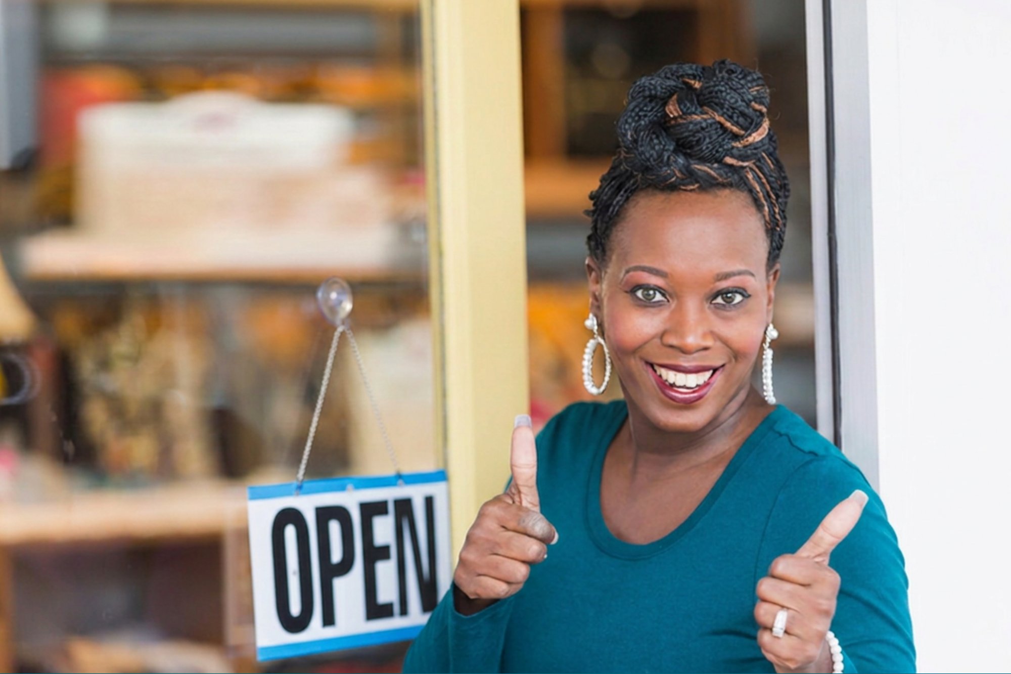 Shop owner standing in front of ther store giving a thumbs-ups