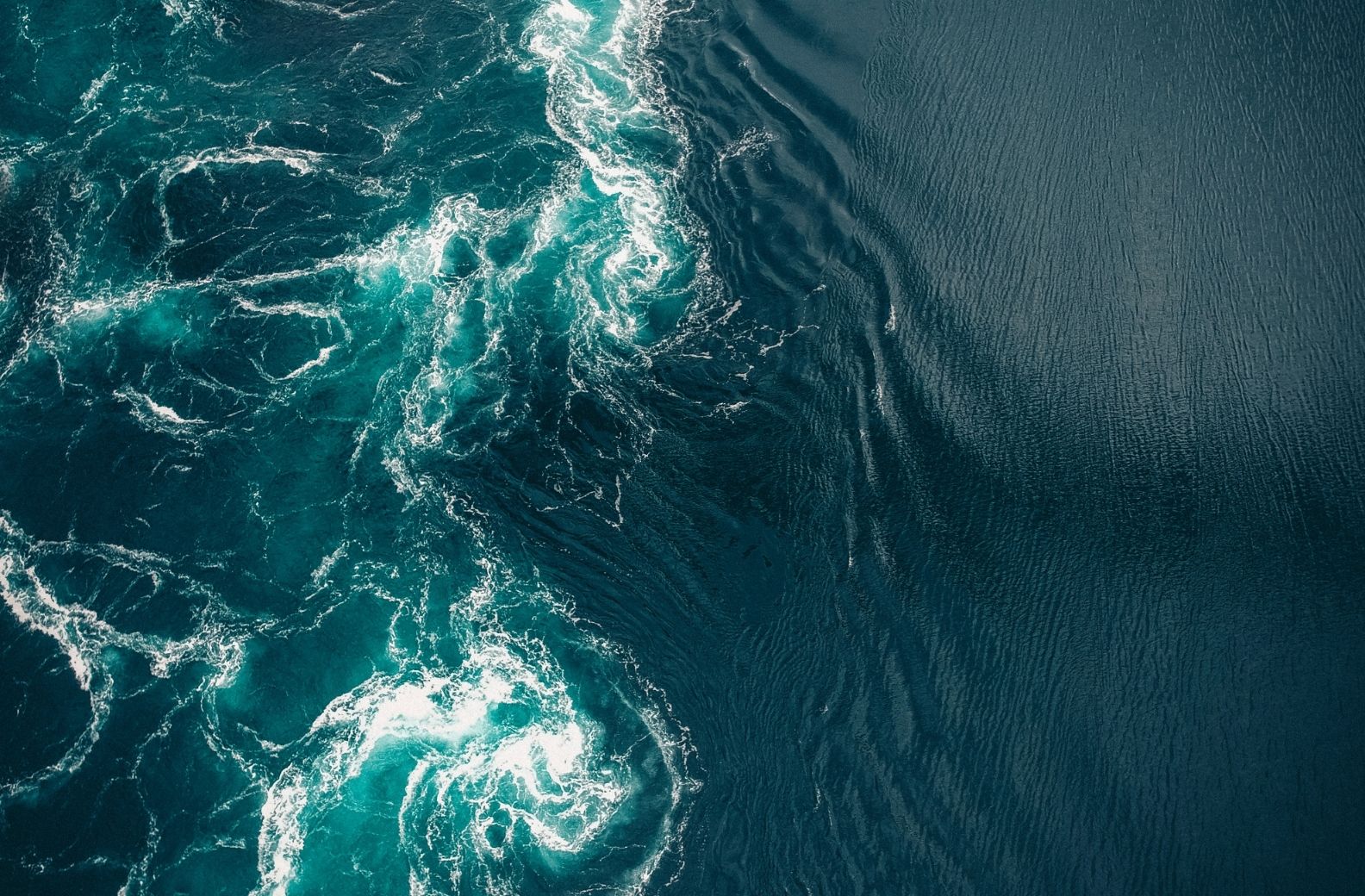 Turquoise water seen from above, rough and rotating on one side where currents move beneath the surface, smooth and flowing on the other.