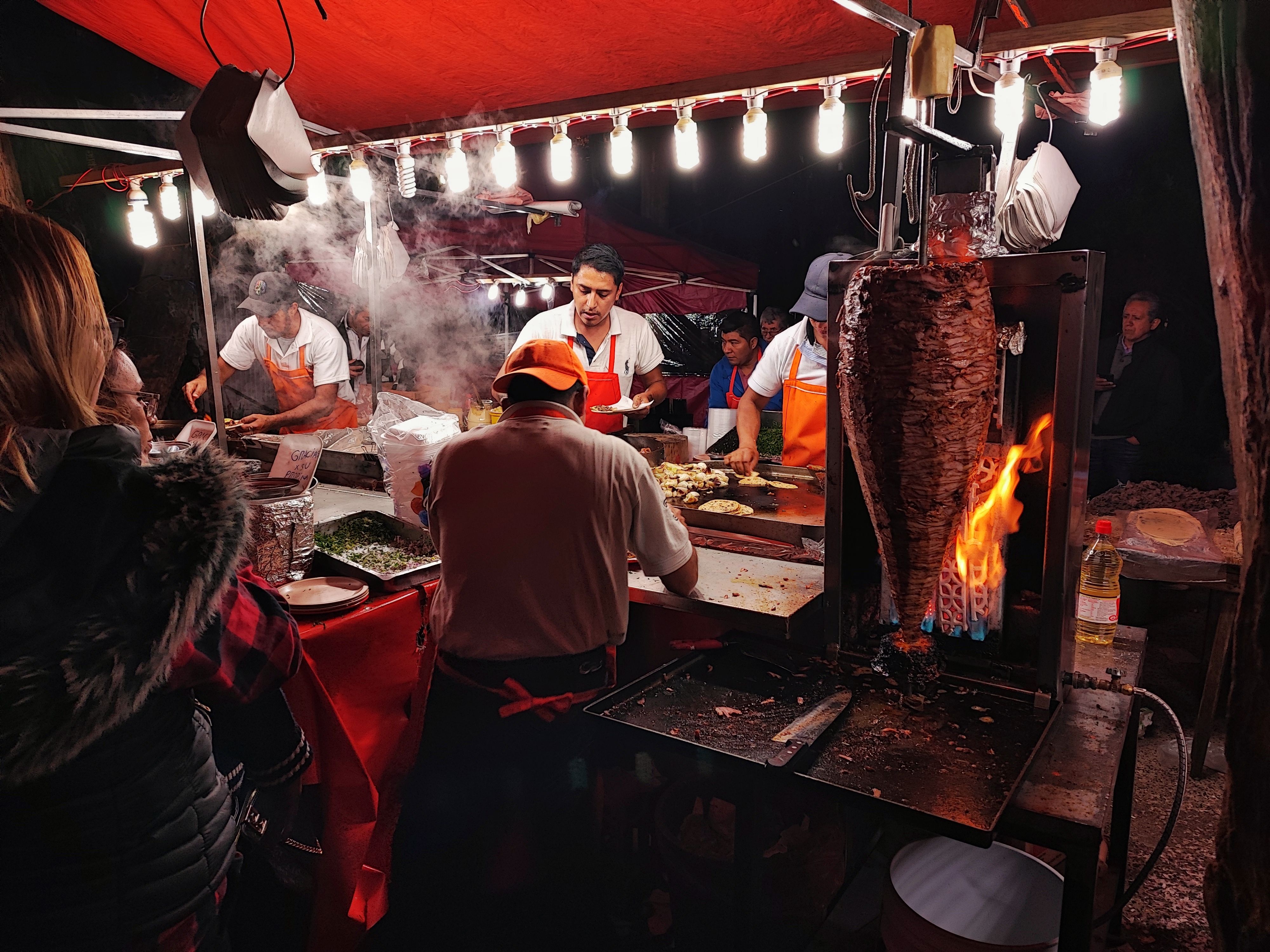 Vendors carving tacos al pastor from a flaming trompo at a Mexico City street stall after dark. Photo by Ritchie Soto on Pexels.