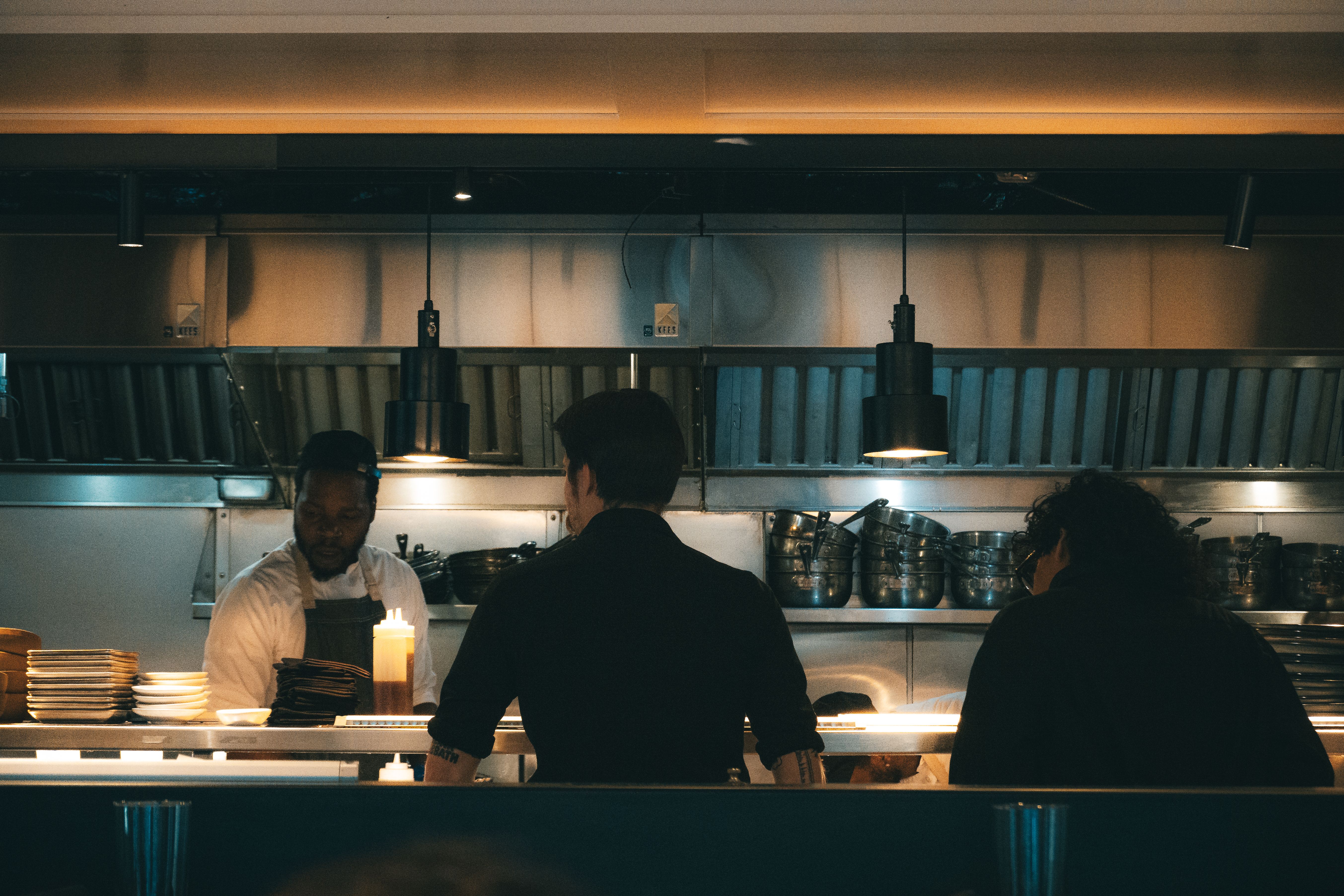 Chefs work the open kitchen line of a New York restaurant in the evening. Photo by Willian Justen de Vasconcellos on Pexels.