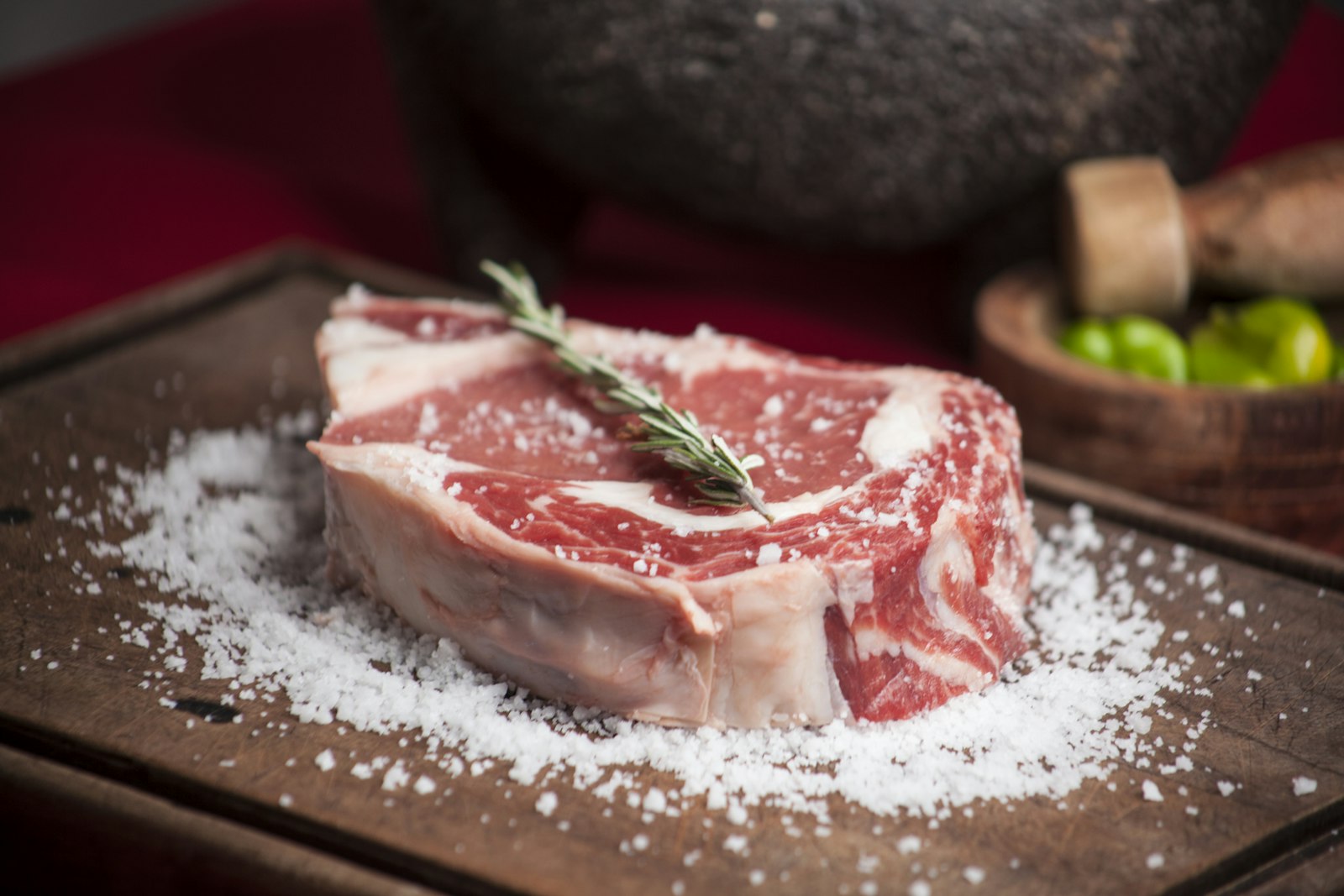 A thick-cut bone-in steak on a butcher's board with coarse salt, ready for the coals. Photo by Edson Saldaña on Unsplash.