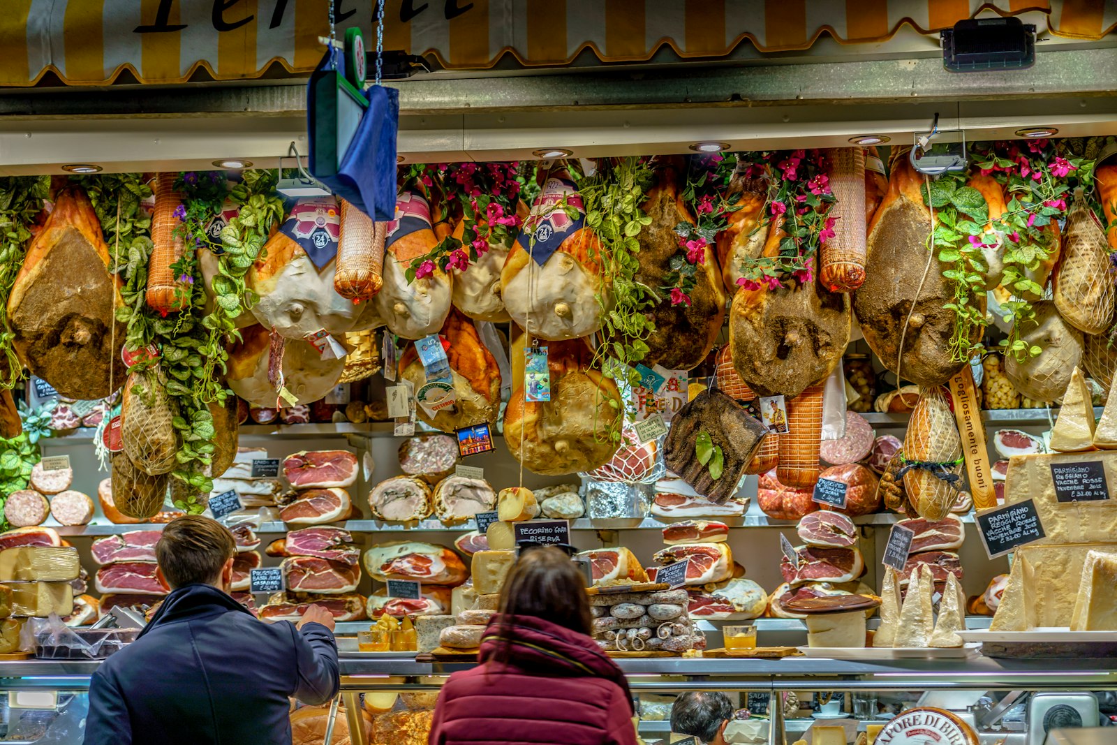 Hams and cheeses hanging over a packed counter at Mercato Centrale in Florence. Photo by Richard Hedrick on Unsplash.