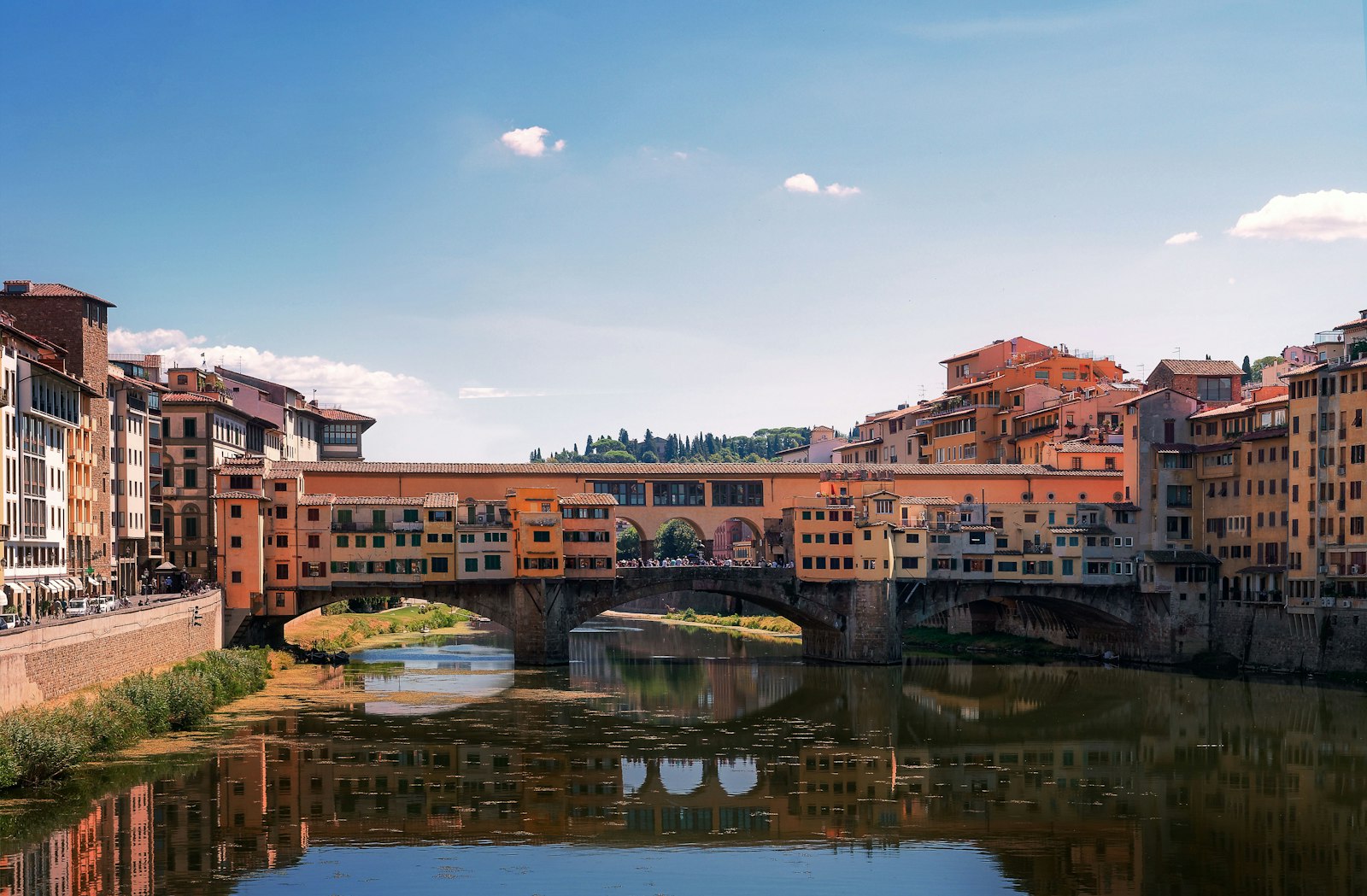 Ponte Vecchio spanning the Arno on a clear day, its goldsmith shops hanging over the river. Photo by Ansgar Scheffold on Unsplash.