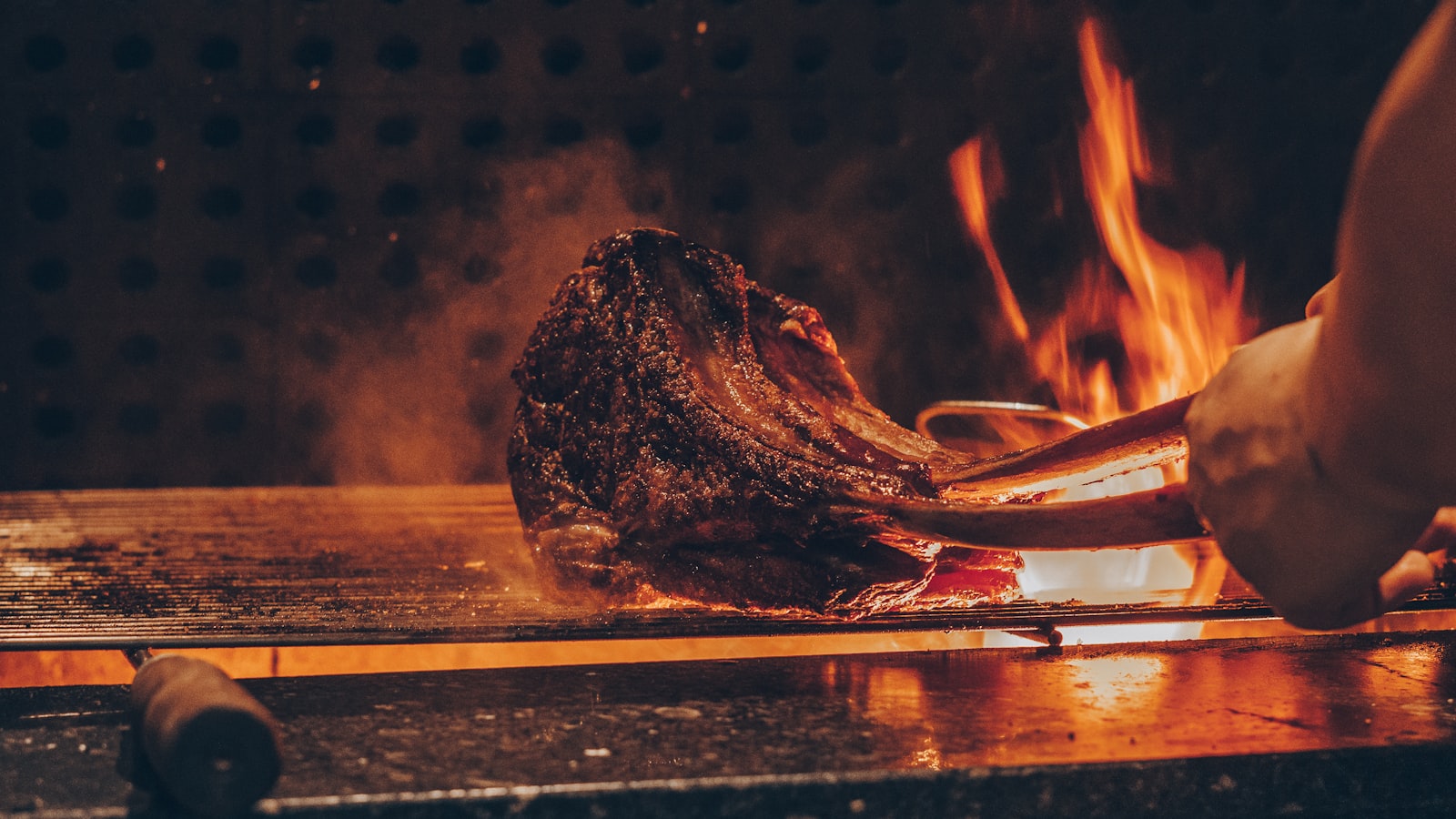 A thick steak searing over open flames on a charcoal grill. Photo by Emerson Vieira on Unsplash.