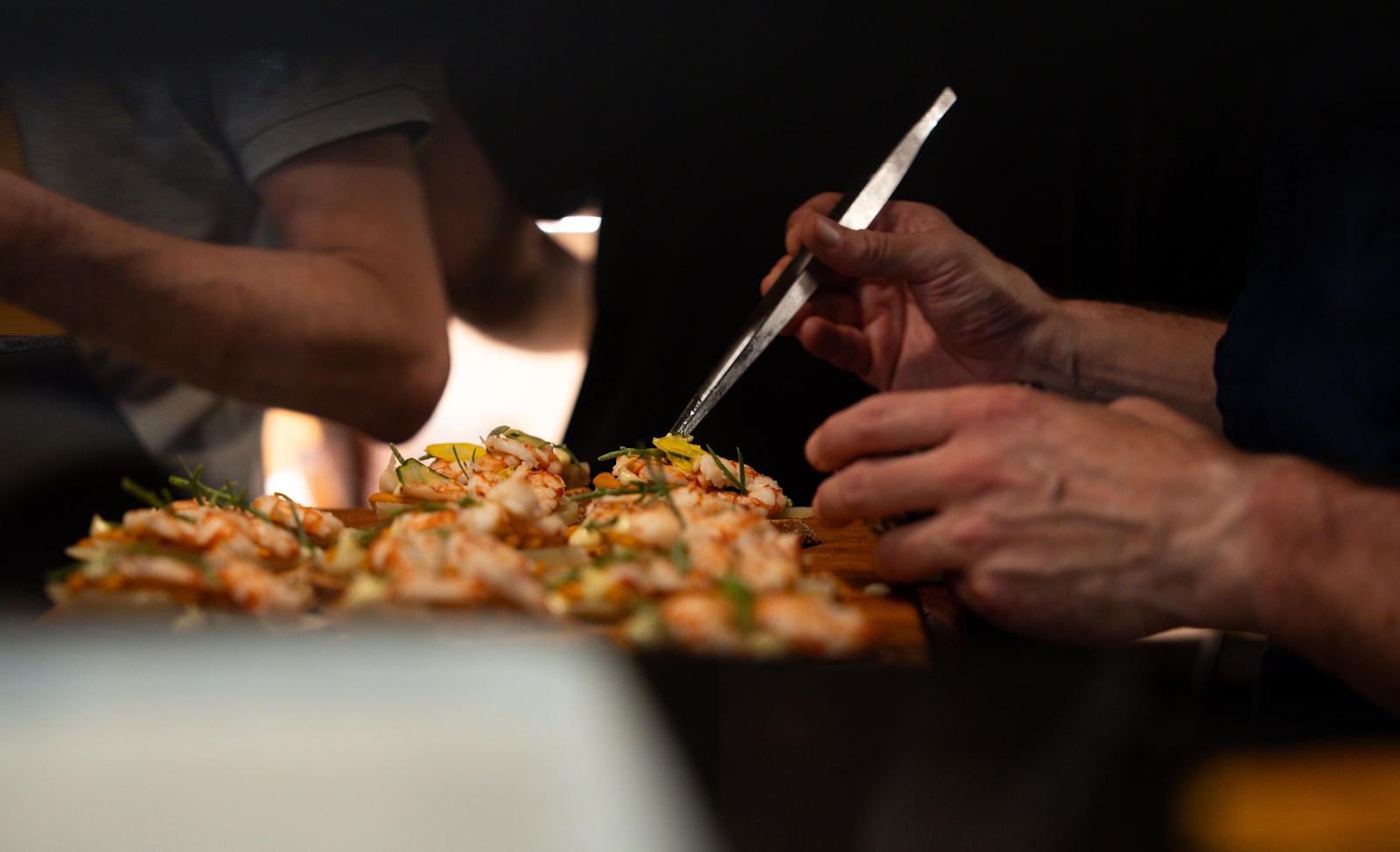 Hands plating a dish in a busy kitchen. Photo by Thibault Lam Tran on Unsplash.