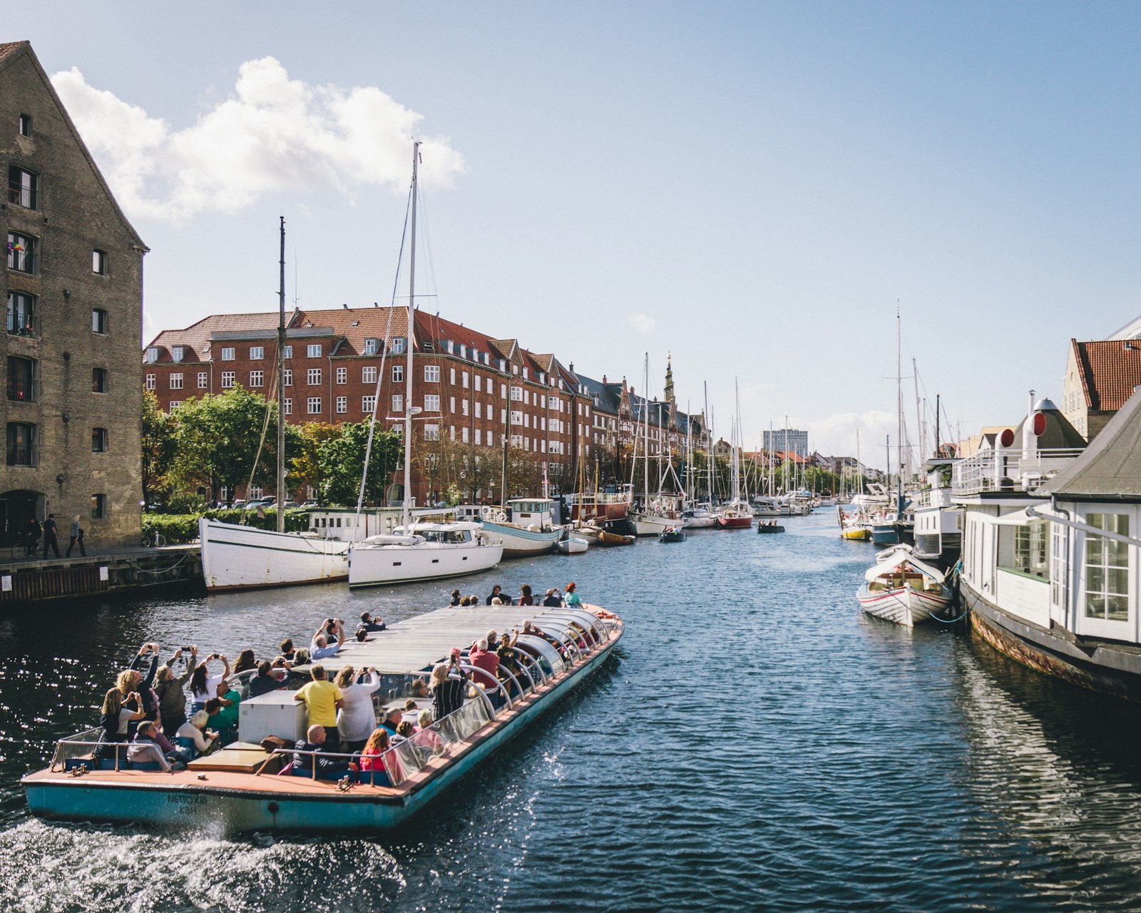 A tour boat full of passengers gliding down the Christianshavn canal in summer. Photo by Kristijan Arsov on Unsplash.