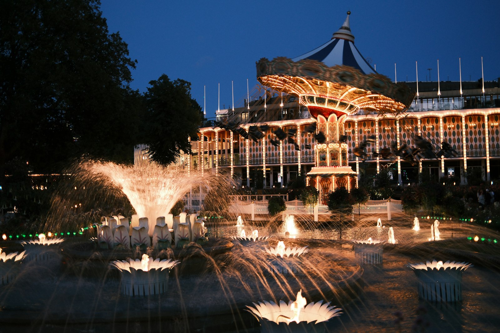 Tivoli's fountains and carousel lit up after dark. Photo by yunfei cai on Unsplash.