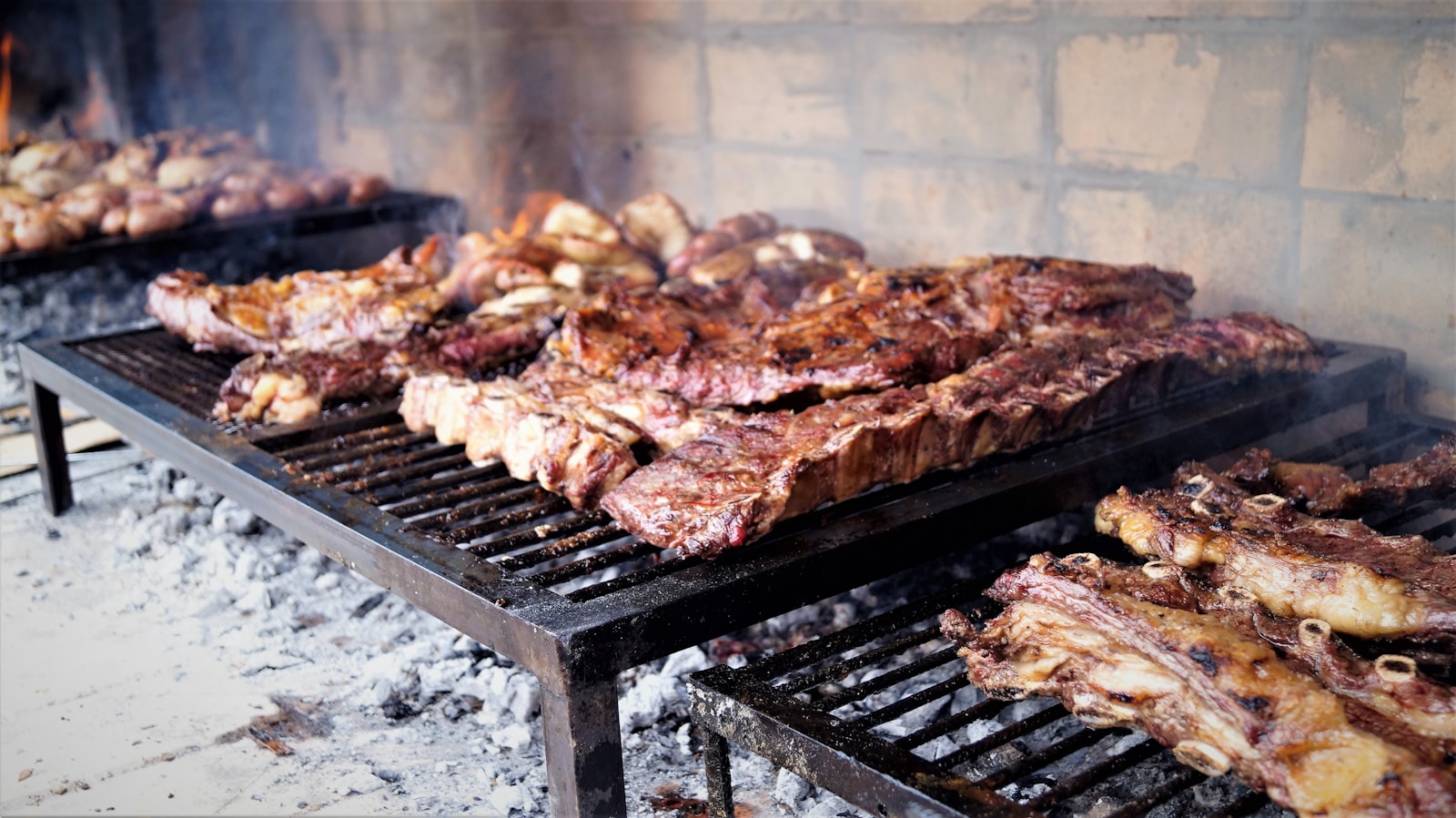 Ribs and sausages cooking over the coals of an Argentine parrilla. Photo by DEBY RODRIGUEZ on Unsplash.