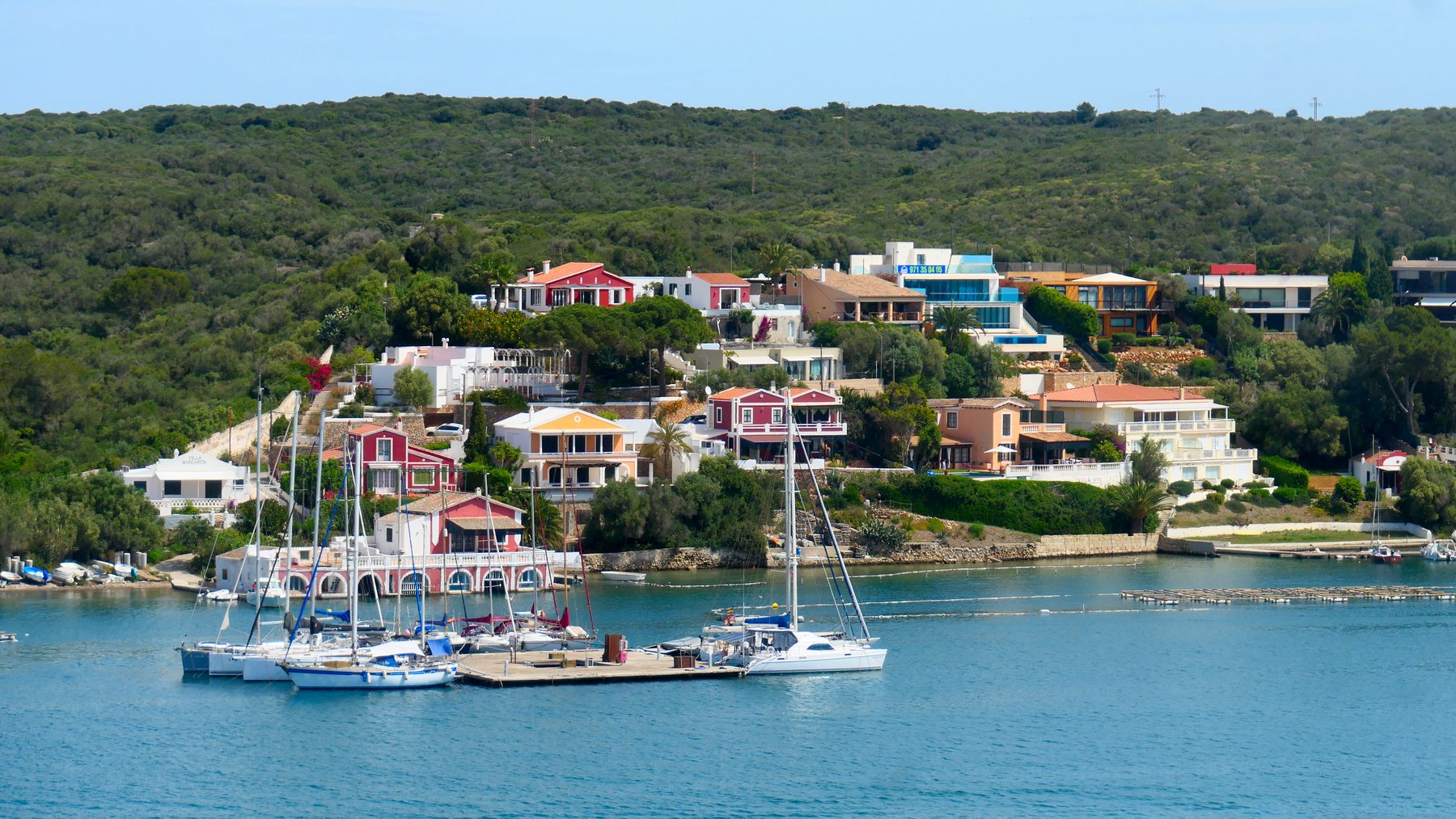 Sailboats moored below the villa-lined shore of Maó's deep natural harbour. Photo by Lukas Lussi on Pexels.