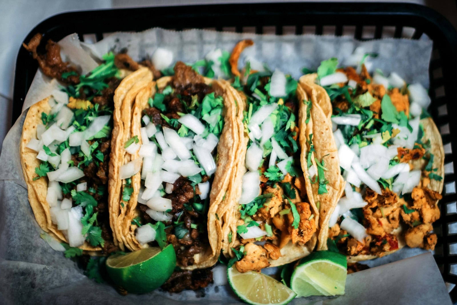 A basket of street tacos topped with onion and cilantro, with lime on the side. Photo by Xavier crook on Unsplash.
